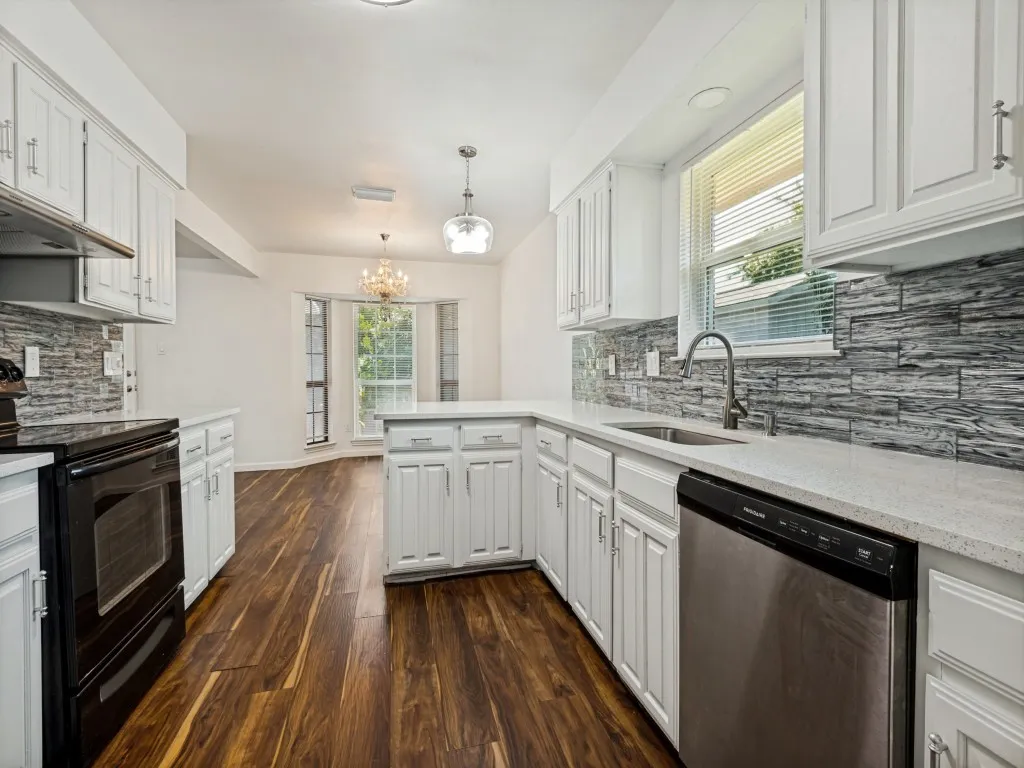 Kitchen featuring white cabinetry, light-toned countertops, a textured backsplash, wood-finish flooring, and stainless steel appliances