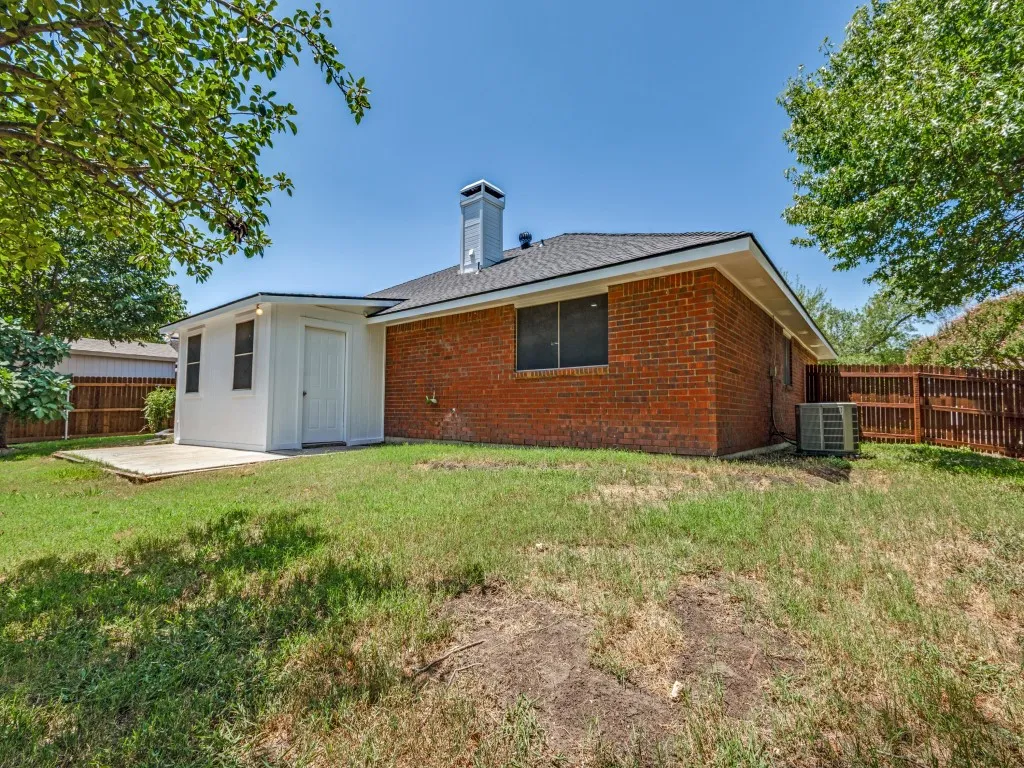 Brick exterior with a white chimney, black shingle roof, and a privacy fence