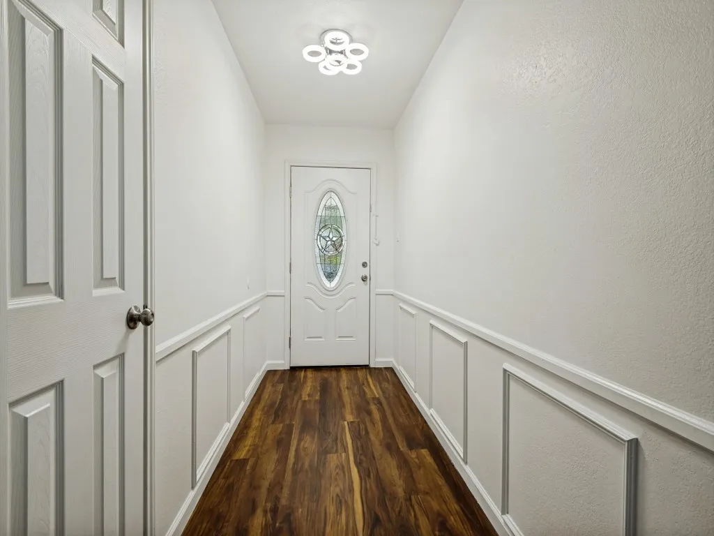Entryway featuring wood-finish flooring, decorative wainscoting, and a front door with an oval stained-glass insert