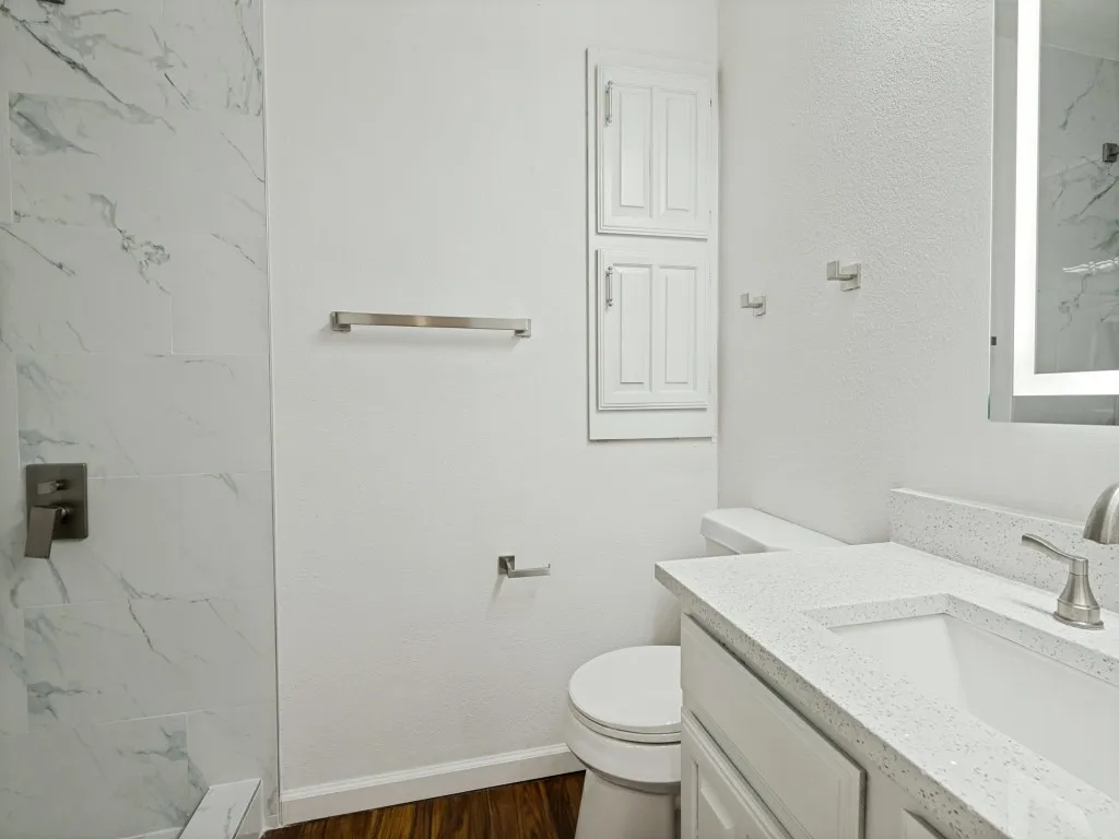 Modern bathroom featuring a tiled shower with a dark finish fixture, wood-finish flooring, built-in wall cabinetry, and a vanity with an integrated sink and light-colored countertop
