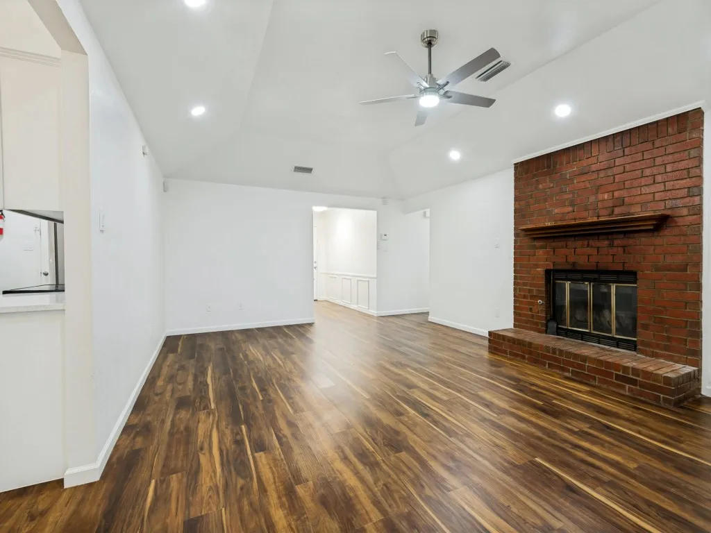 Wood-finish flooring throughout, brick fireplace with a hearth and mantel, vaulted ceiling with recessed lighting, and a ceiling fan