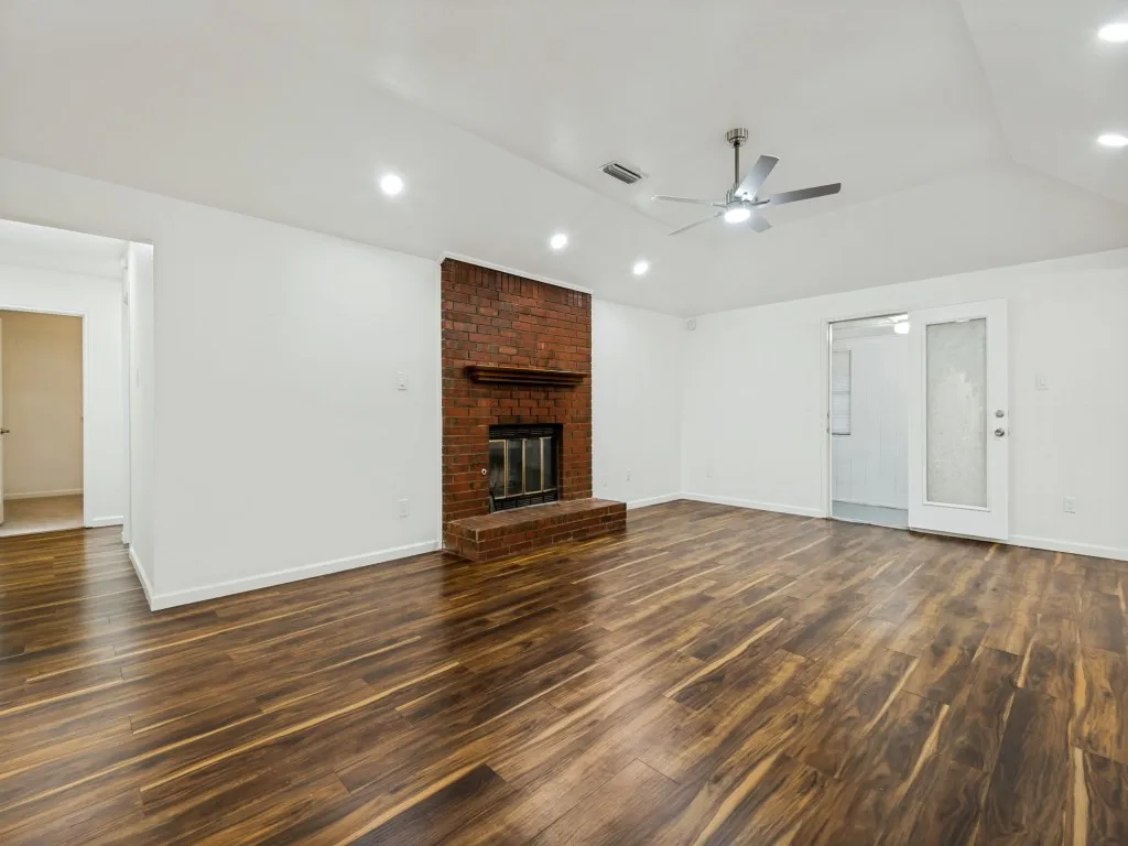Expansive room featuring wood-finish flooring, a brick fireplace with a wood mantle, a ceiling fan, recessed lighting, and a glass-paneled door