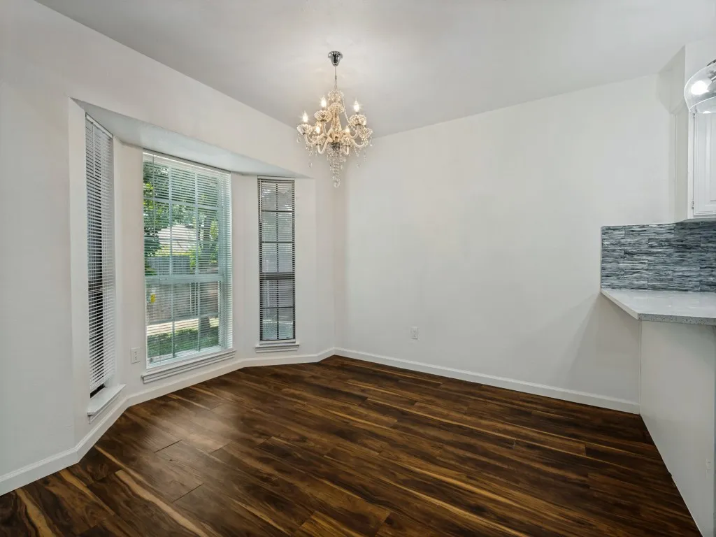 Bay window with multiple panels, wood-finish flooring, elegant chandelier, and a stone-finish backsplash