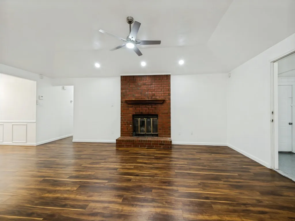 Vaulted ceiling with recessed lighting, wood-finish flooring, brick fireplace with wood mantel, and wainscoting detail