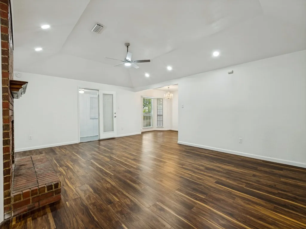 Spacious living area featuring wood-finish flooring, a brick fireplace, a vaulted ceiling with recessed lighting, and a ceiling fan