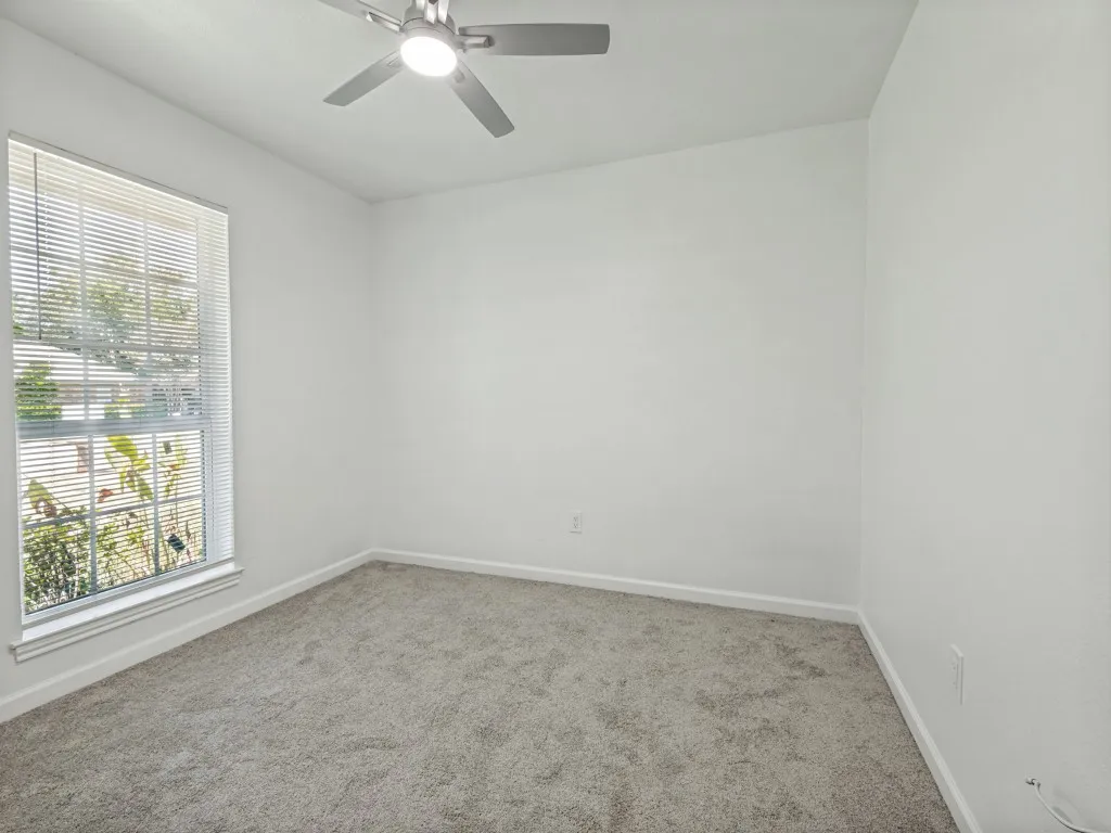Neutral-toned carpeting, white walls, and a window with blinds providing natural illumination
