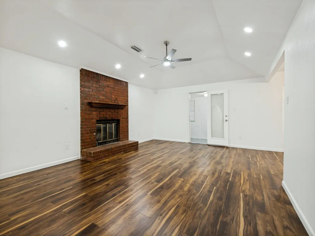 Brick fireplace with an extended hearth, wood-finish flooring, vaulted ceiling, recessed lighting, and a ceiling fan