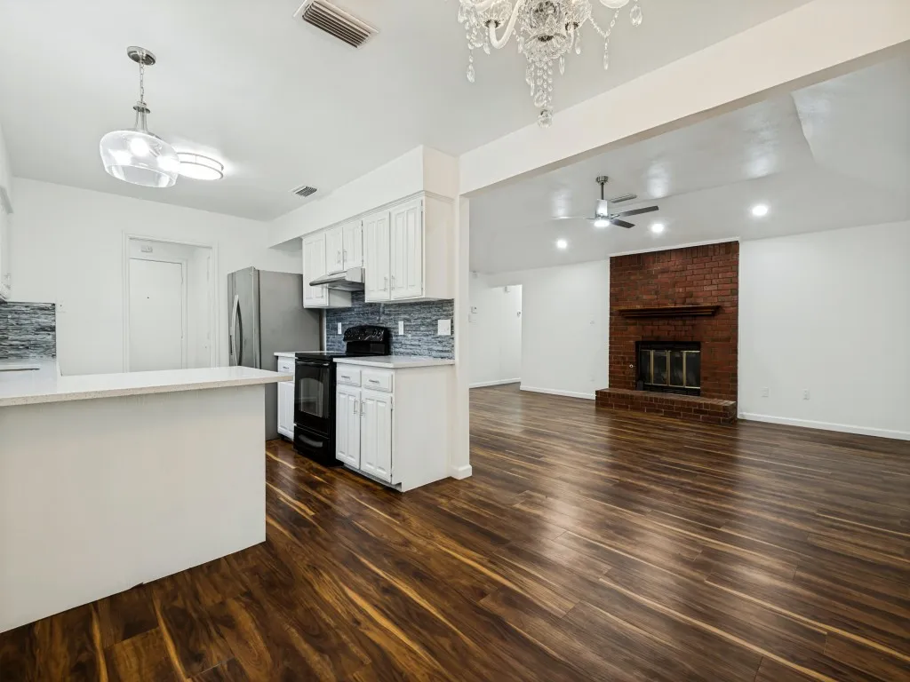 Wood-finish flooring throughout, white cabinetry, integrated stainless steel appliances, brick fireplace, and recessed lighting