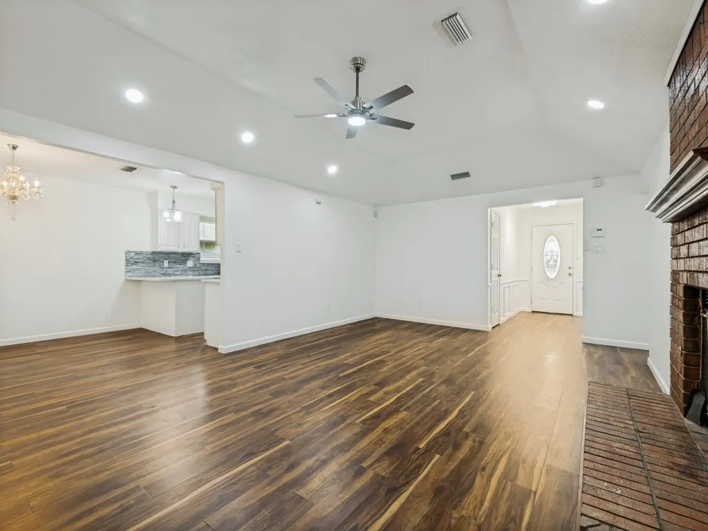 Vaulted ceiling with recessed lighting, wood-finish flooring, brick fireplace, and a ceiling fan