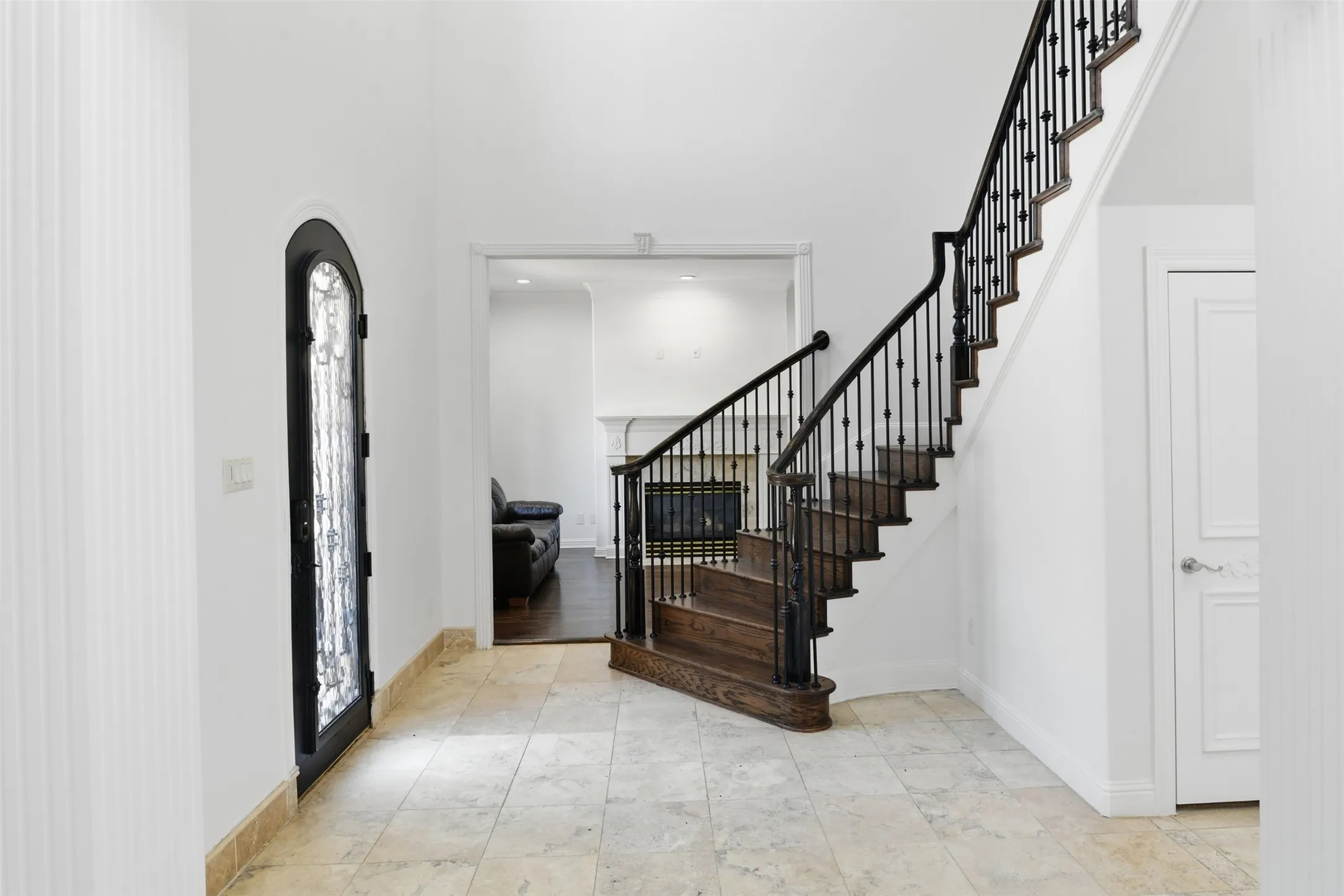 Two-story entryway featuring a custom arched door with decorative glass, curved wood staircase with wrought iron balusters, and large format tile flooring