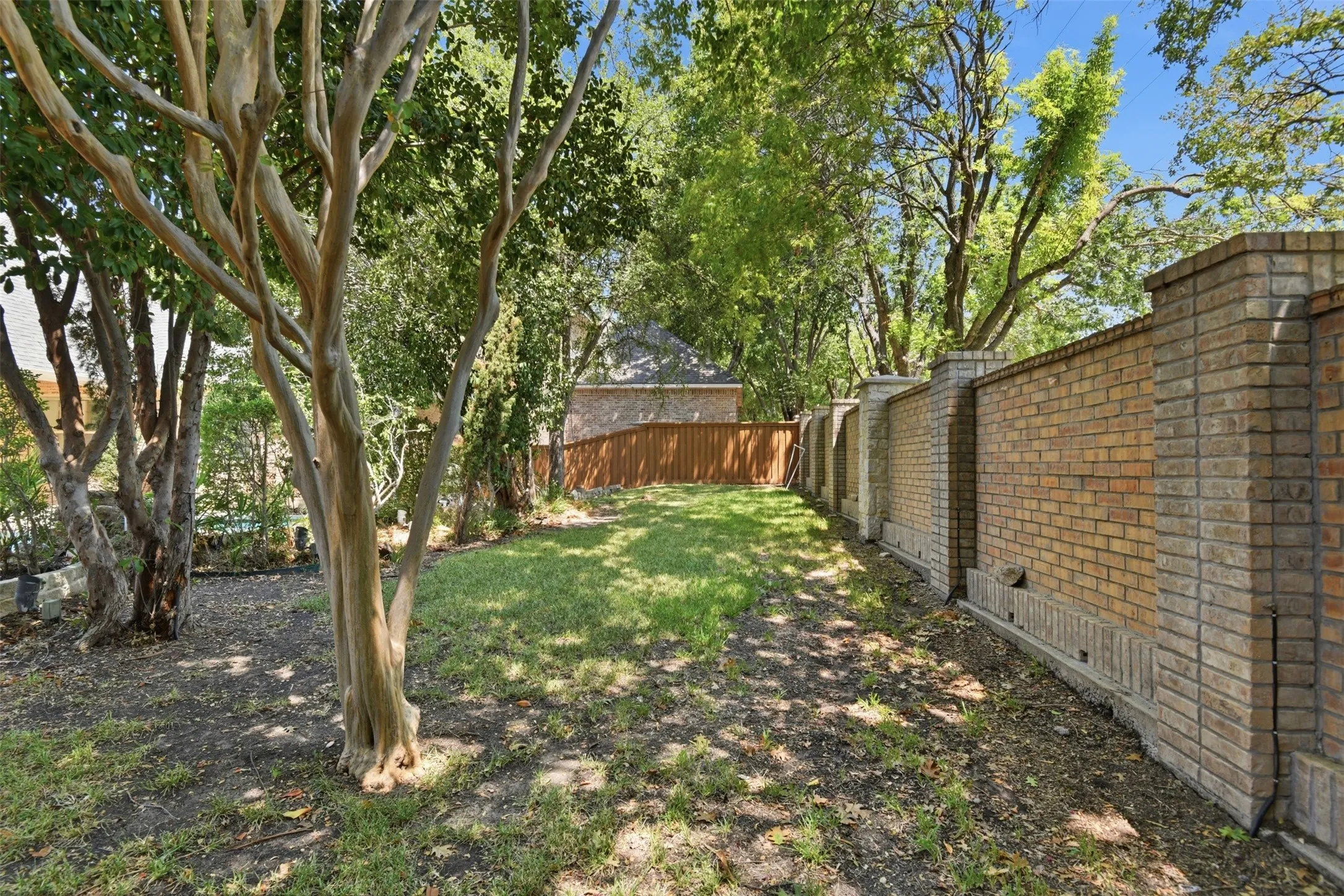 Expansive yard featuring mature trees, a manicured lawn, and a brick privacy wall