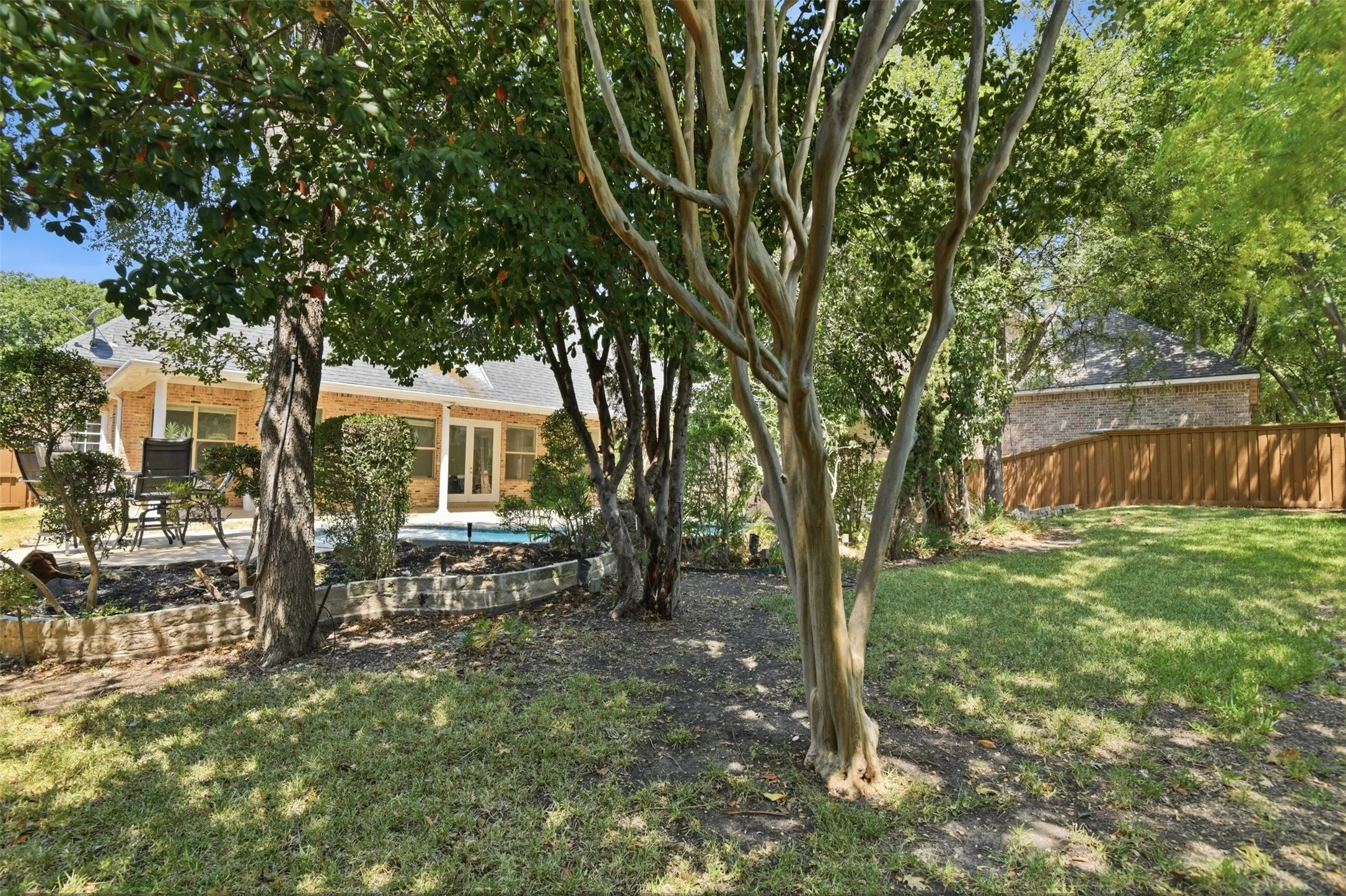 Expansive backyard with a manicured lawn, established trees, and a brick privacy wall