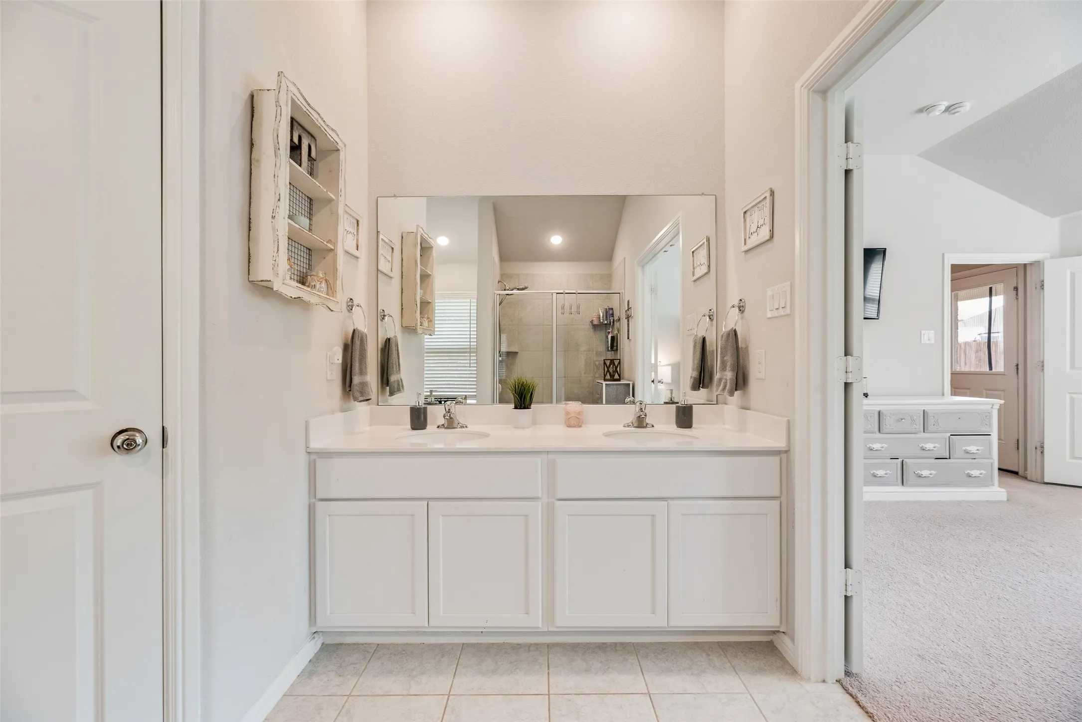 Dual vanity with white cabinetry and integrated sinks, a large wall-mounted mirror, and tile flooring