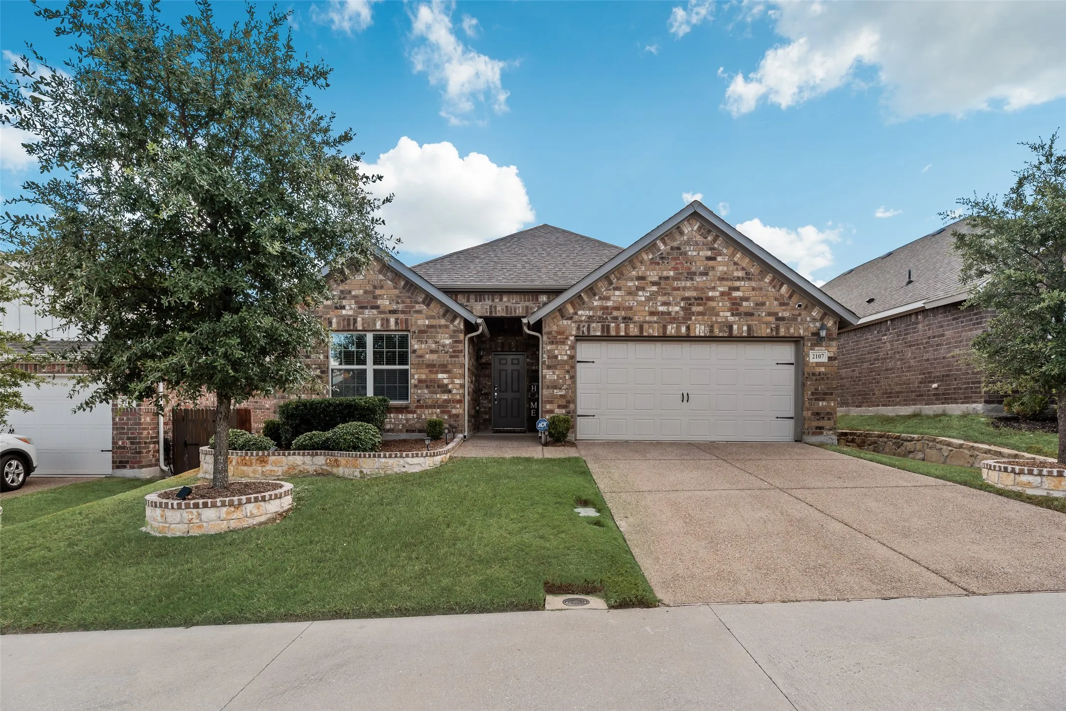 Brick facade, attached garage, concrete driveway, front lawn, and mature trees