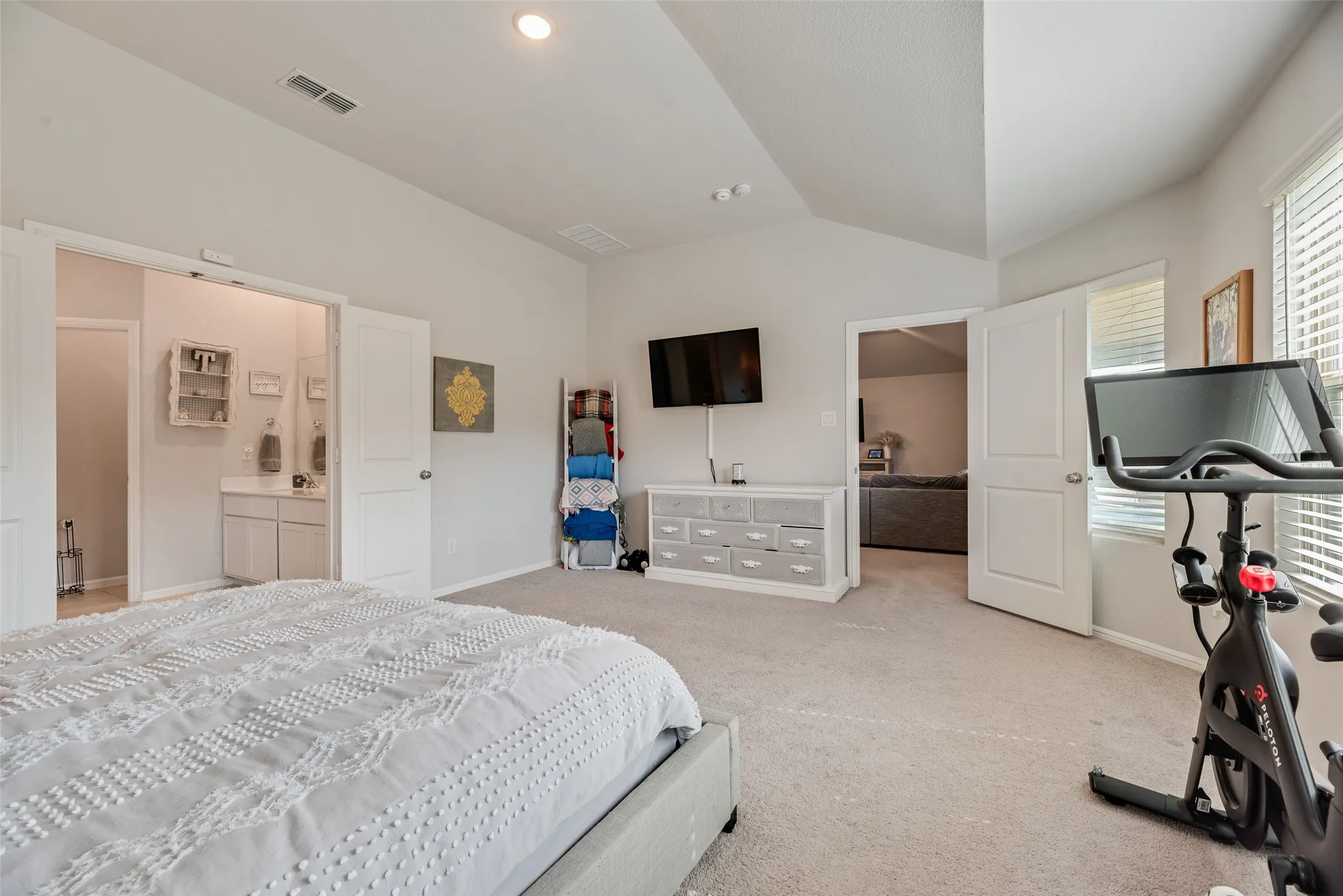 Vaulted ceiling with recessed lighting, light-toned carpeting, white shaker-style vanity with dual sinks, and white paneled doors