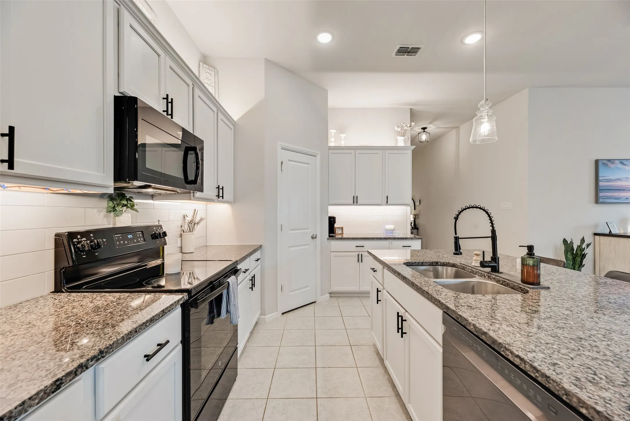 White cabinetry with black hardware, stone countertops, stainless steel appliances, tile flooring, and recessed lighting
