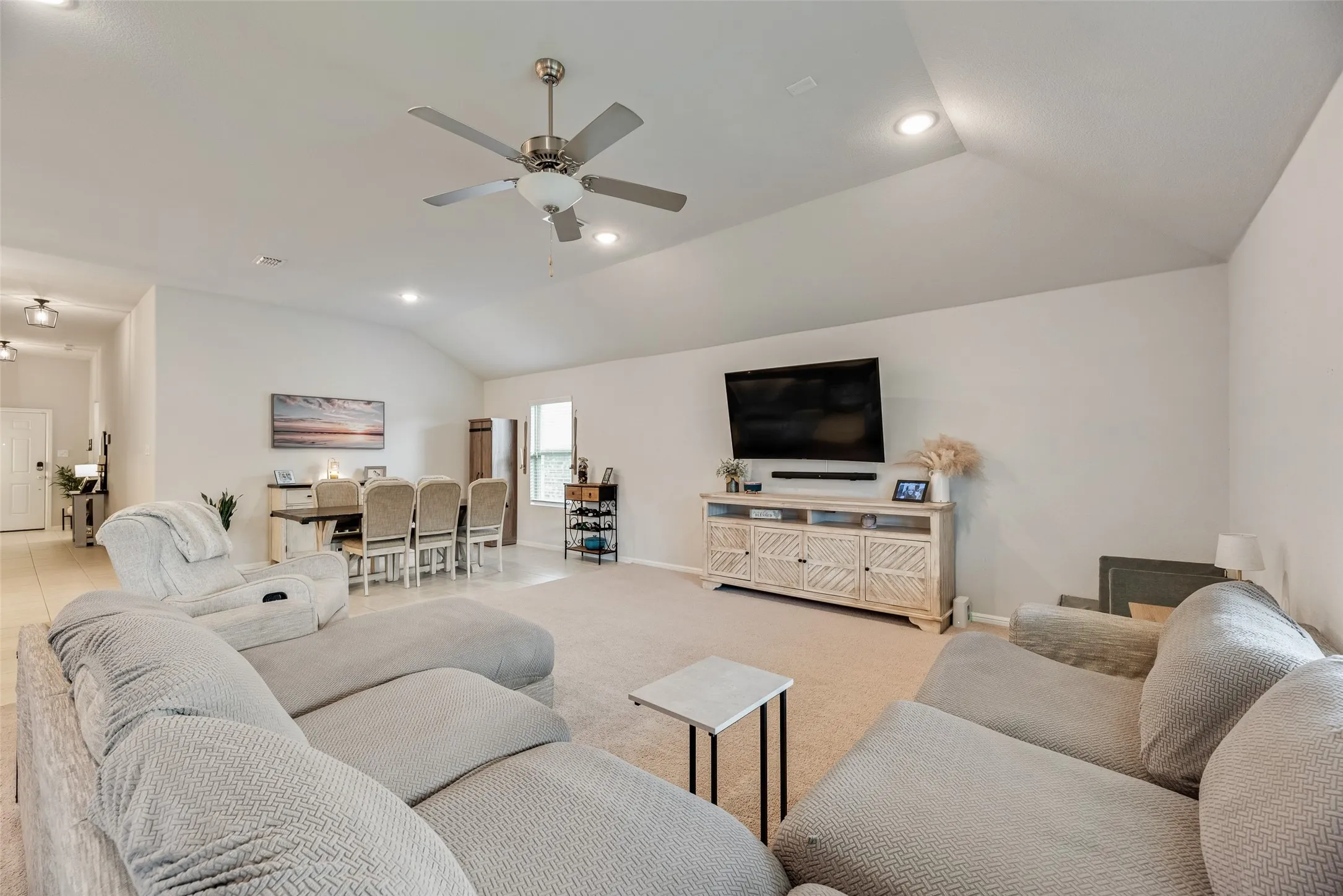 Vaulted ceiling with recessed lighting, ceiling fan, carpeted living area, tiled dining area, and a built-in media console