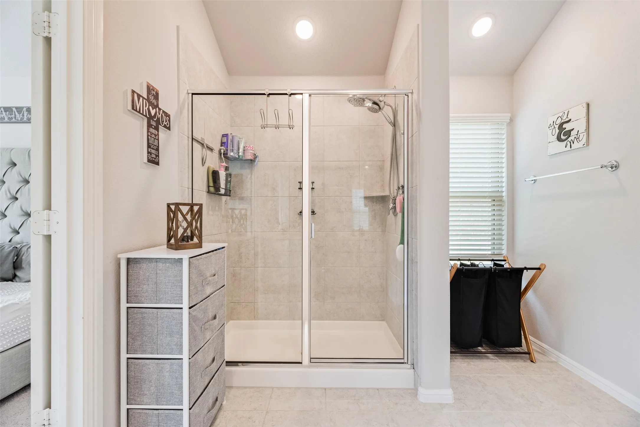 Glass-enclosed shower with a tiled surround, recessed lighting, and a window with blinds