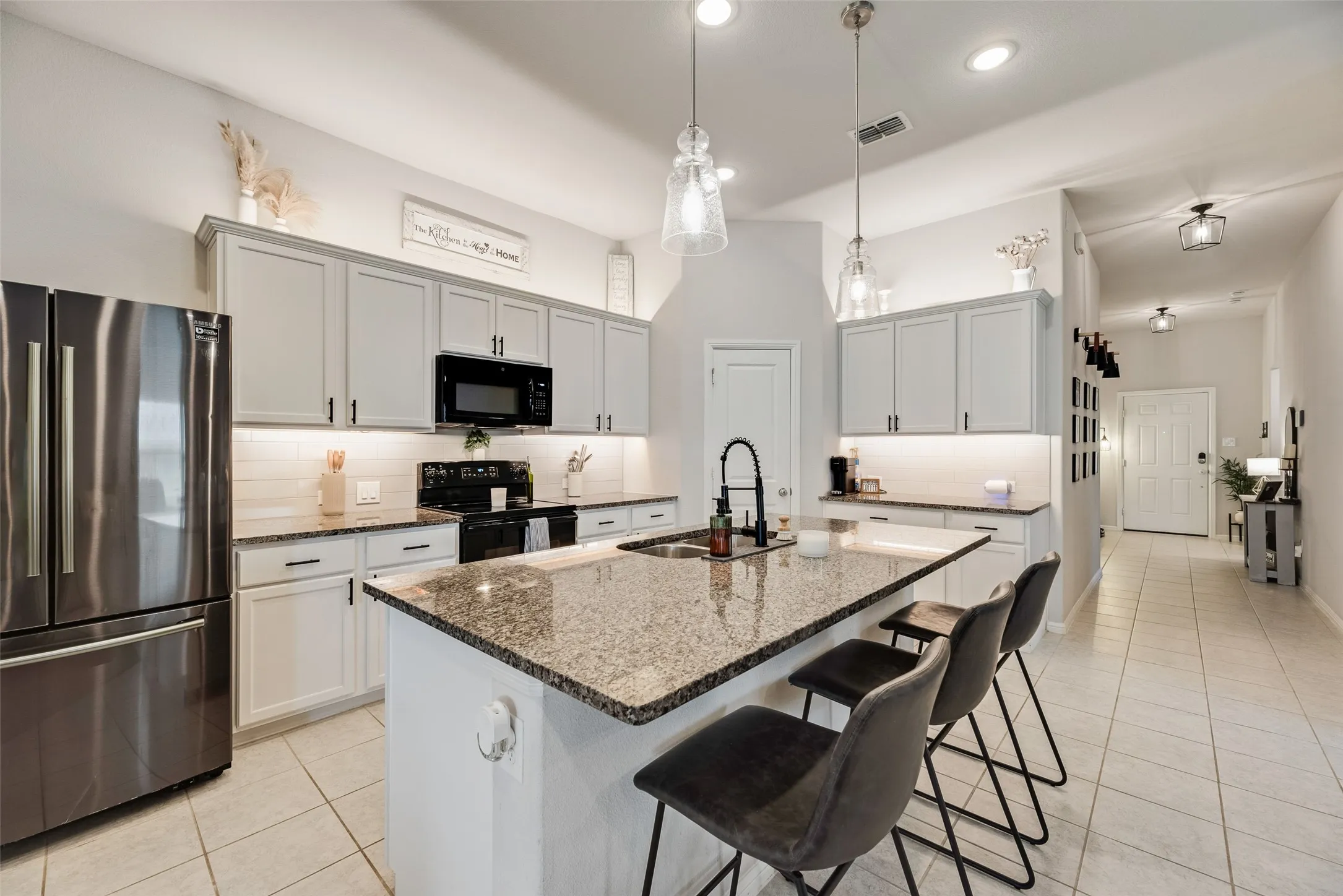 Kitchen featuring a large island with a natural stone countertop, white shaker-style cabinetry, stainless steel appliances, and tile flooring