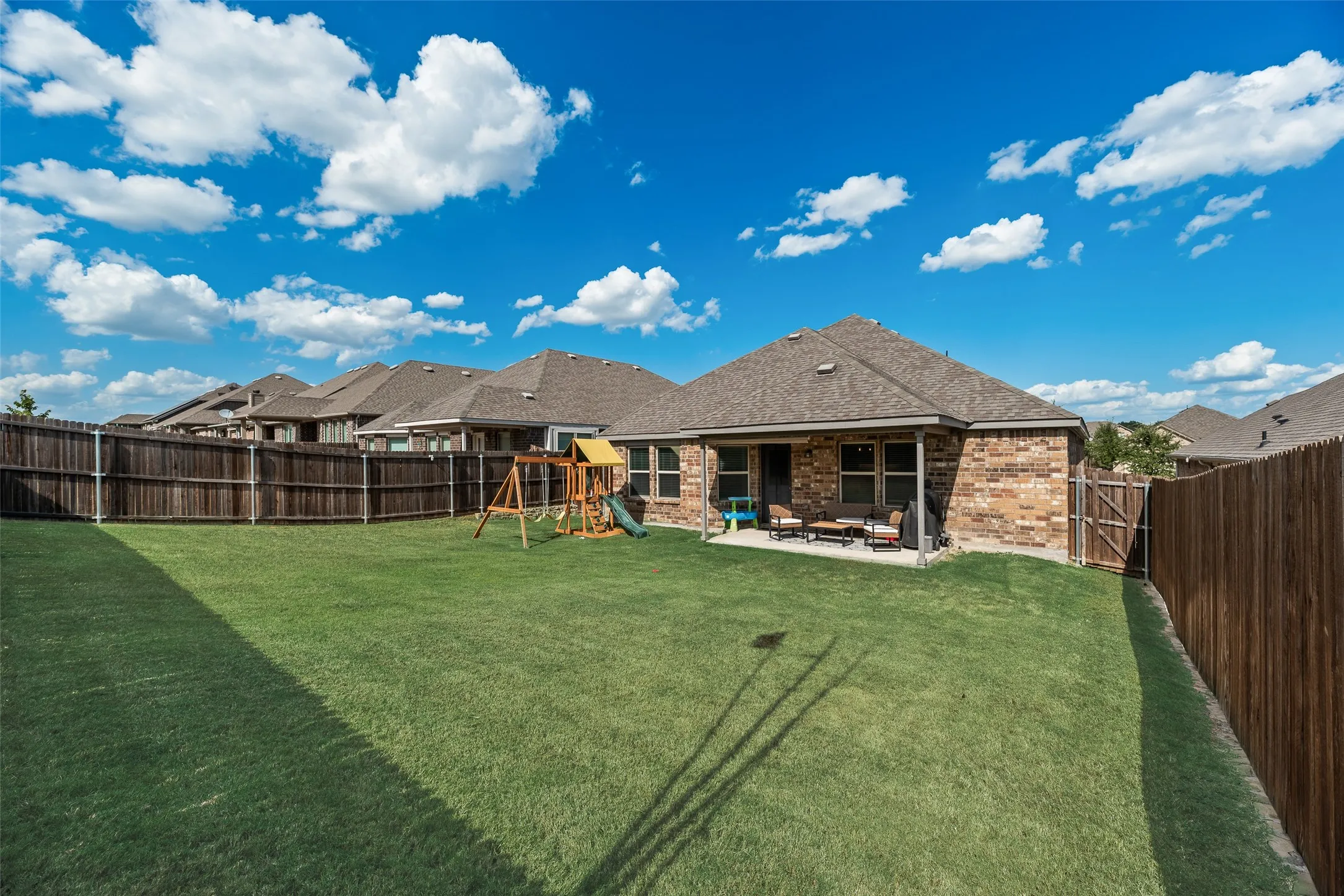 Expansive backyard featuring a manicured lawn, full privacy fencing, and a covered patio