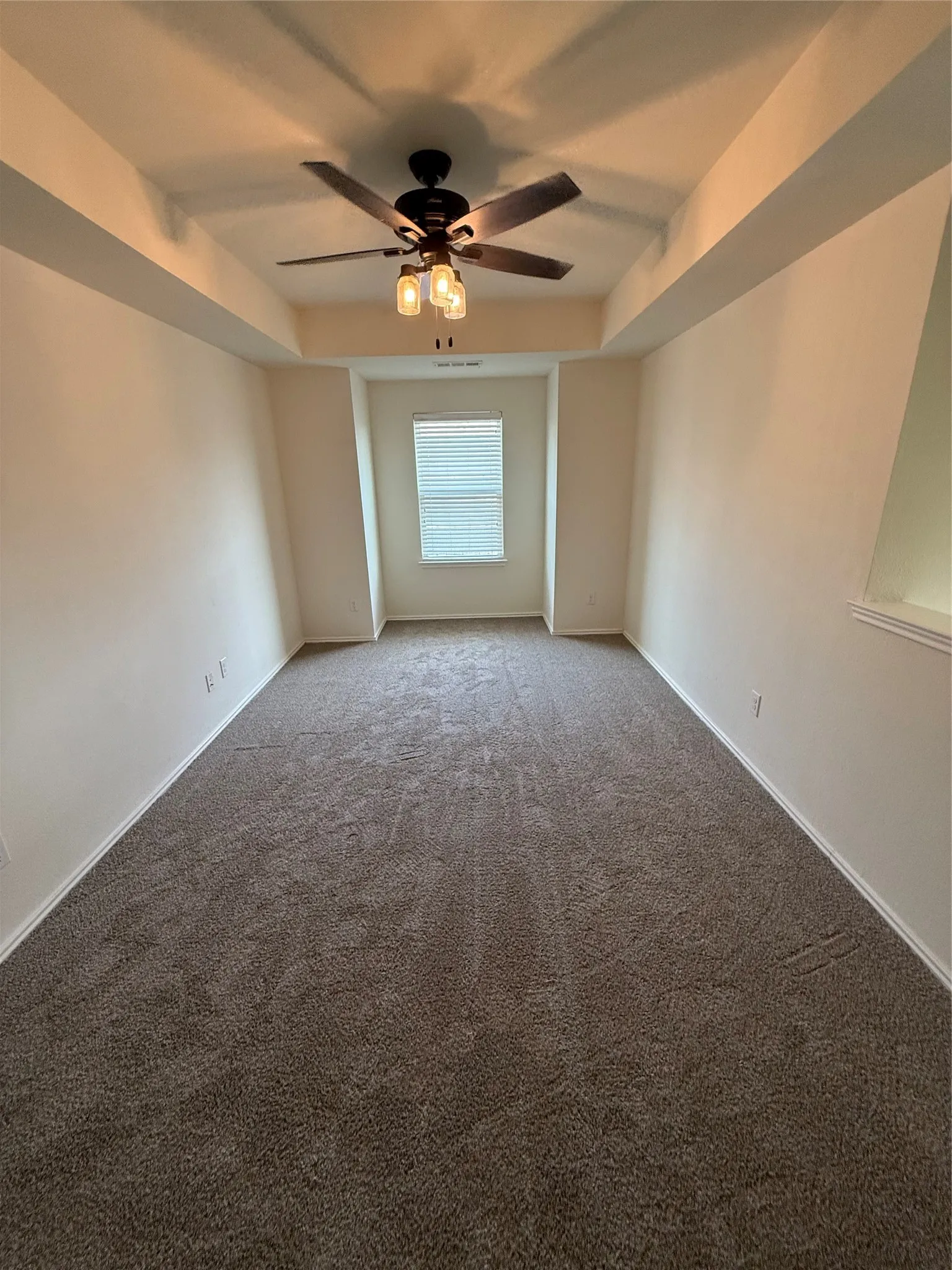 Tray ceiling with a decorative ceiling fan, window with blinds, and wall-to-wall carpeting