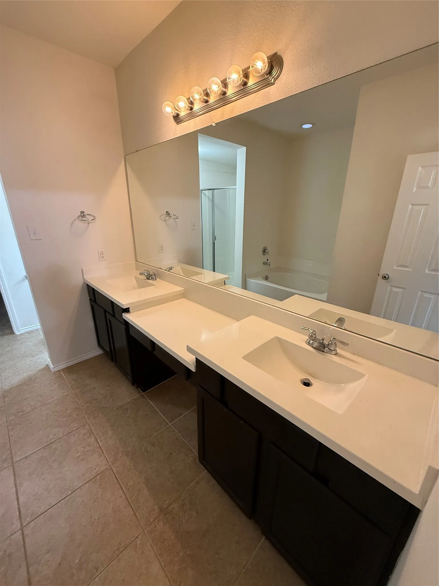 Dual sink vanity with dark wood-finish cabinetry, light-toned countertops, and a full-width mirror