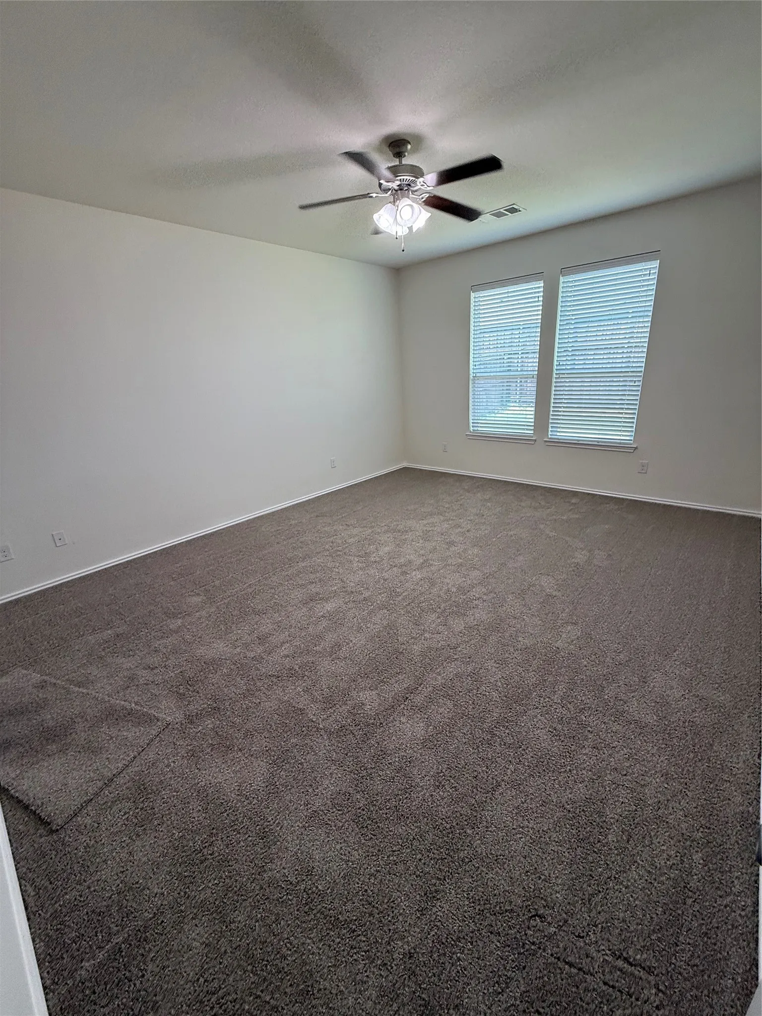 Spacious room featuring neutral carpeting, light-toned walls, and two windows with blinds