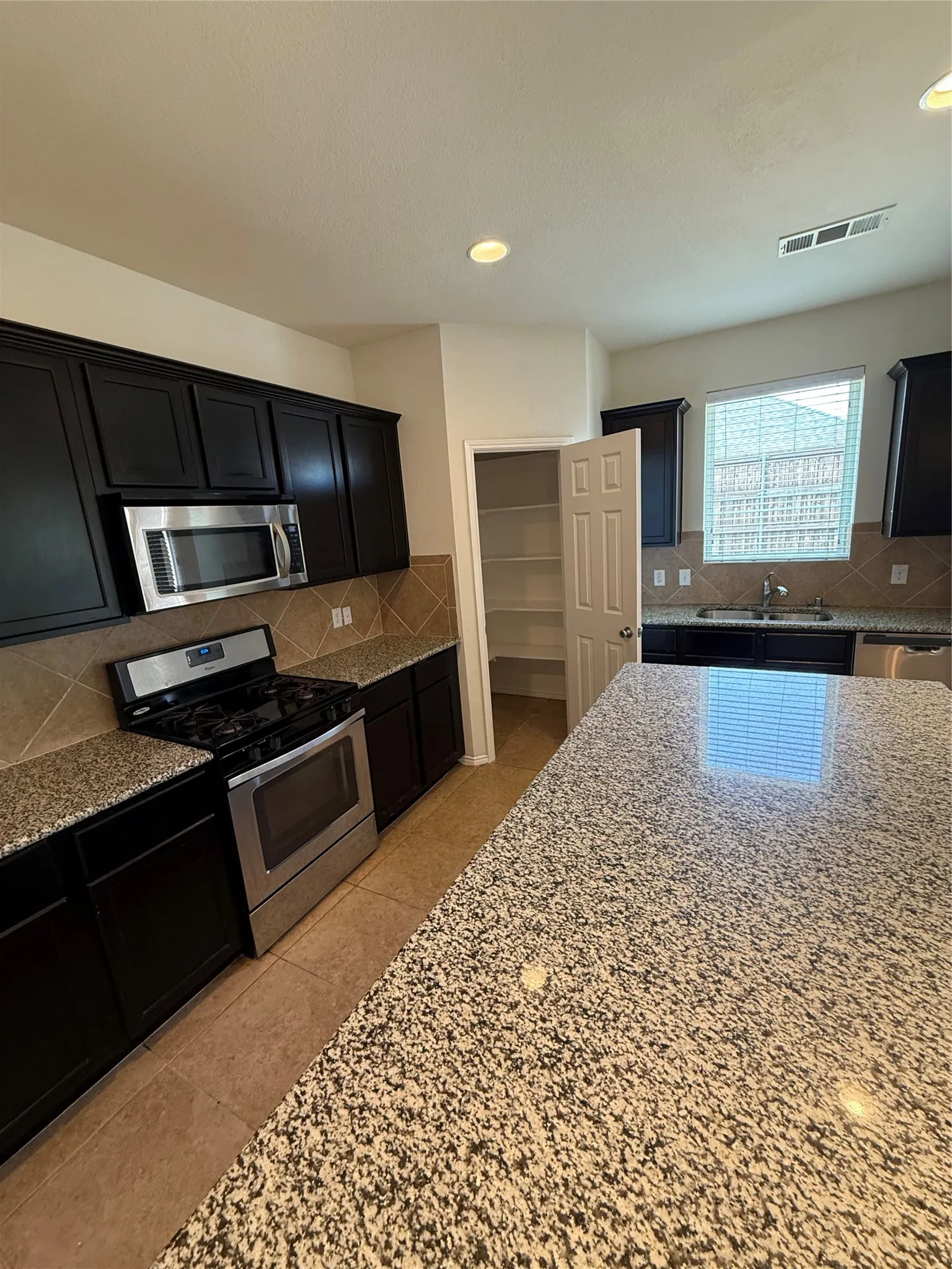 Kitchen featuring dark wood-finish cabinetry, stainless steel appliances, speckled stone countertops, and tile flooring
