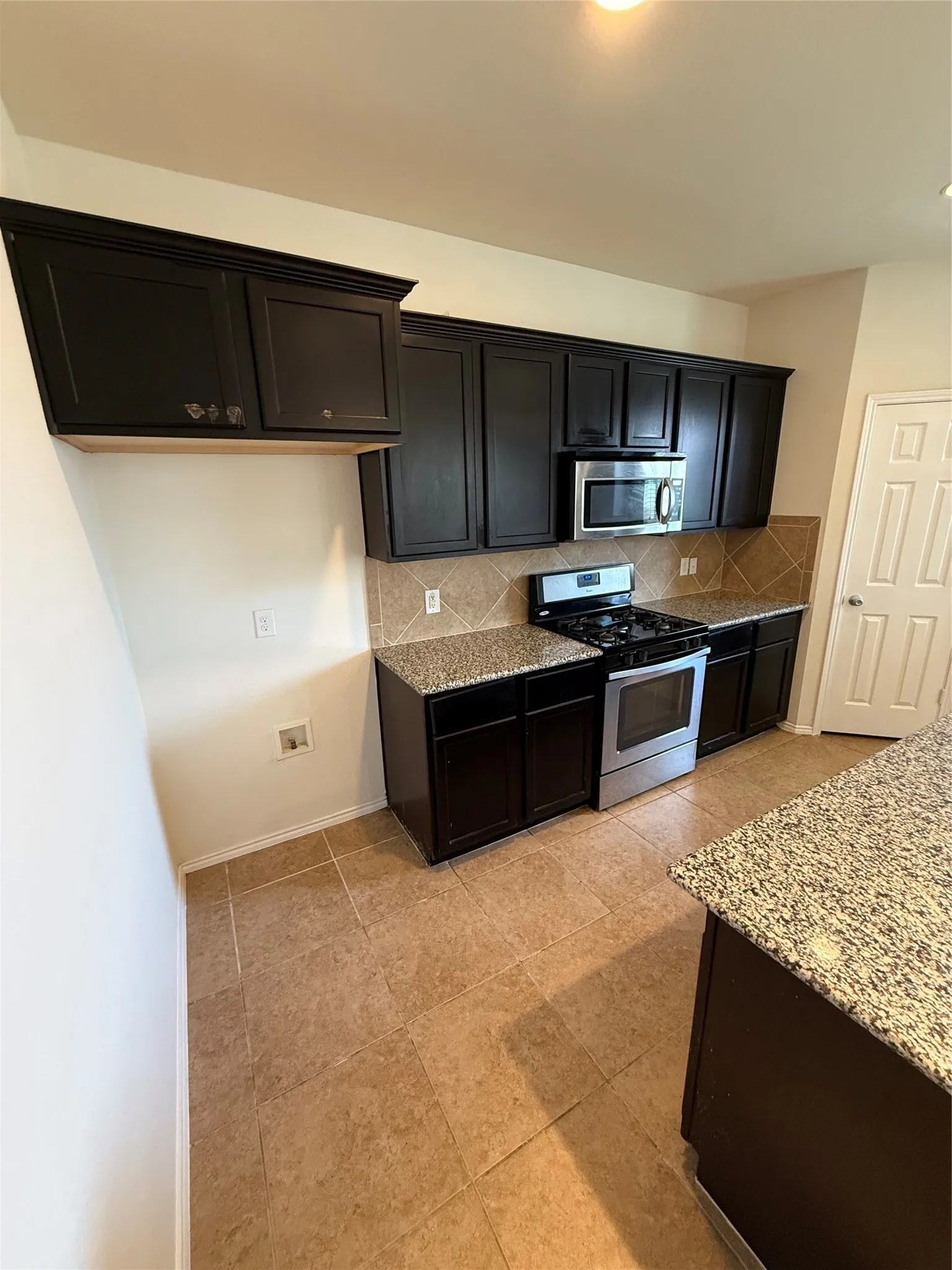 Kitchen featuring dark wood cabinetry, stainless steel oven and microwave, stone-finish countertops, tile backsplash, and tile flooring