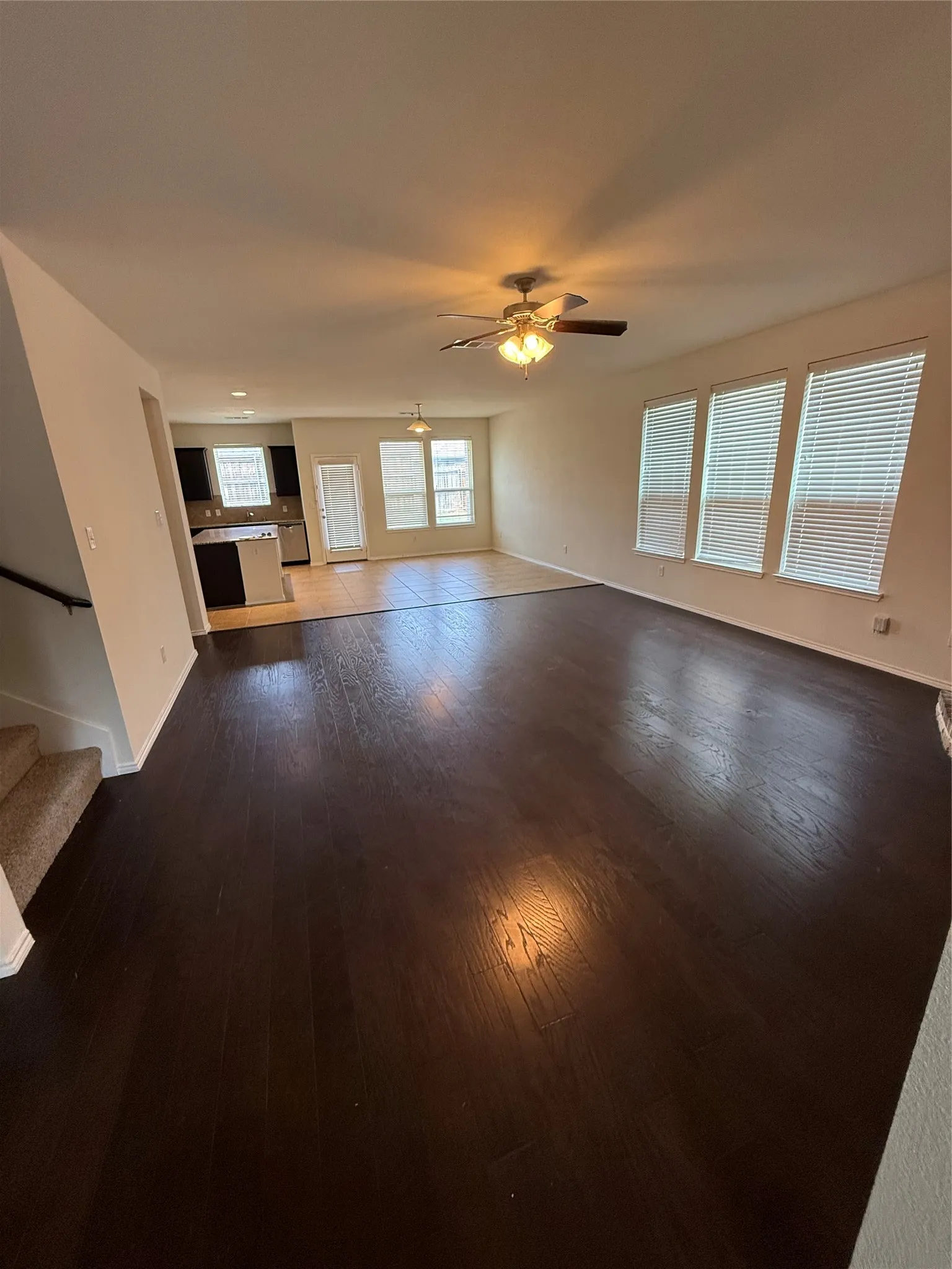 Expansive open-concept living area featuring dark wood-finish flooring, multiple windows with blinds, and ceiling fans