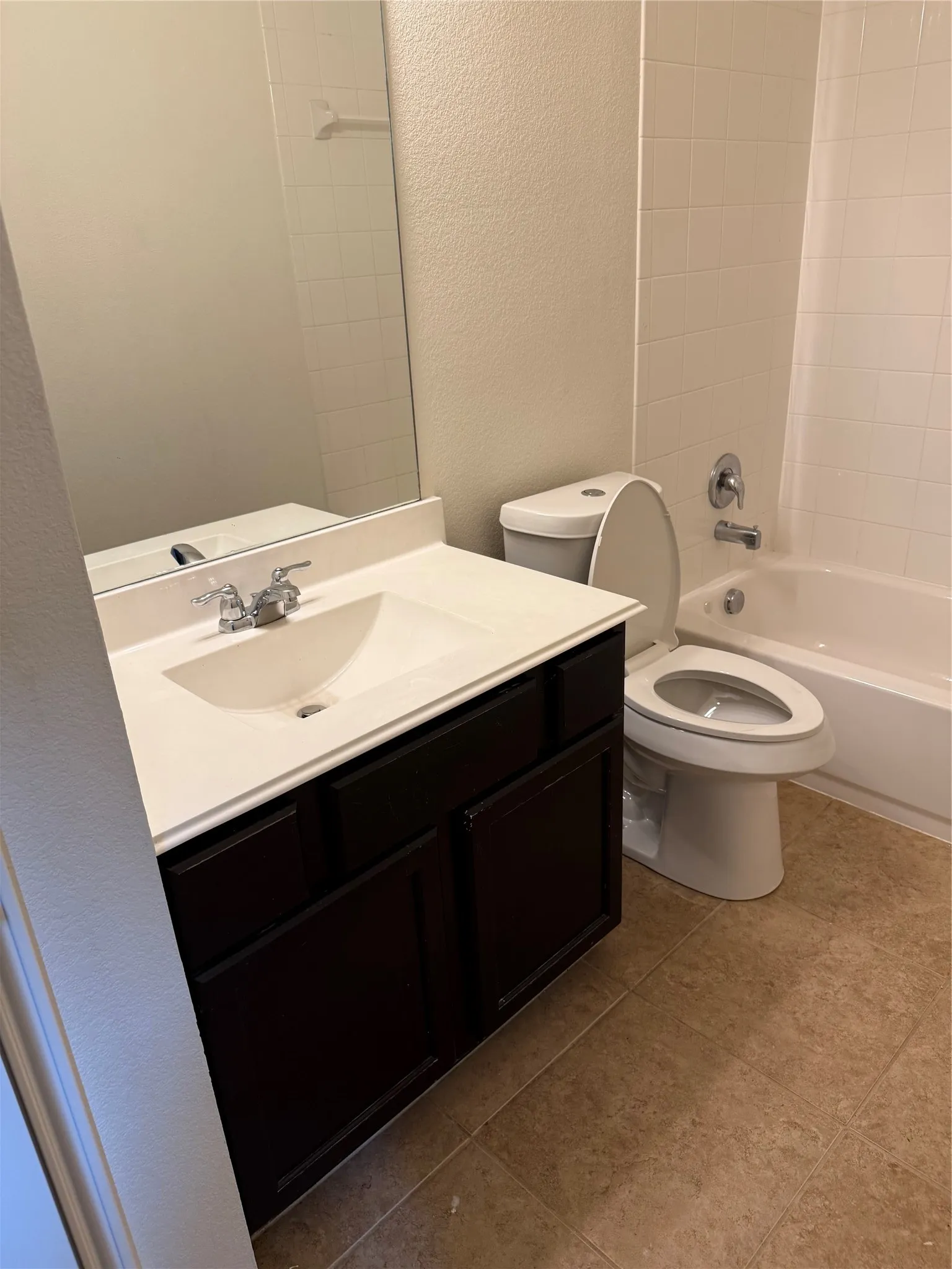 Bathroom featuring a dark wood-finish vanity, integrated sink, large wall-mounted mirror, white subway tile shower surround, and neutral floor tile