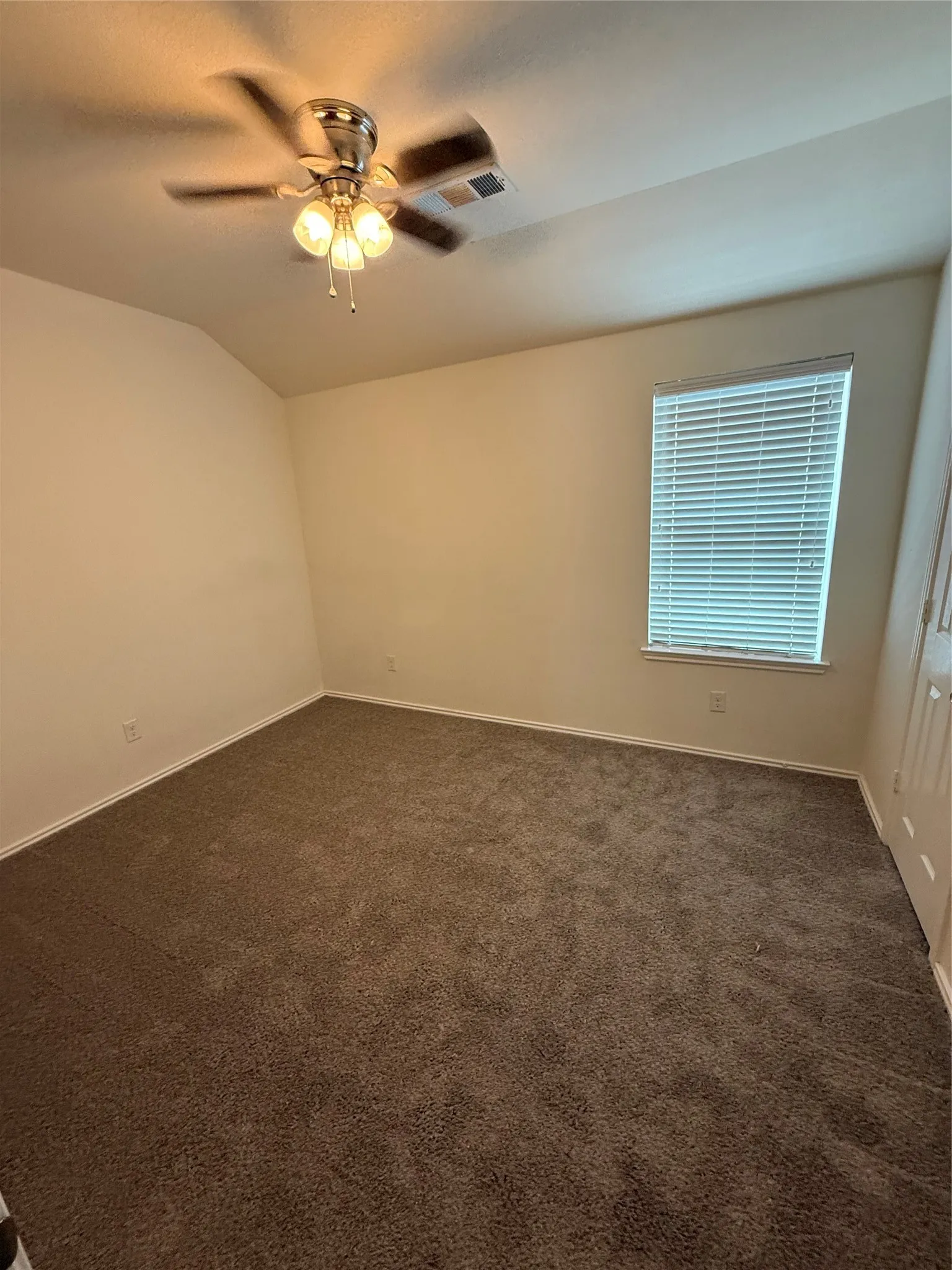 Neutral wall tones, ceiling fan with integrated lighting, carpeted flooring, and a window with blinds