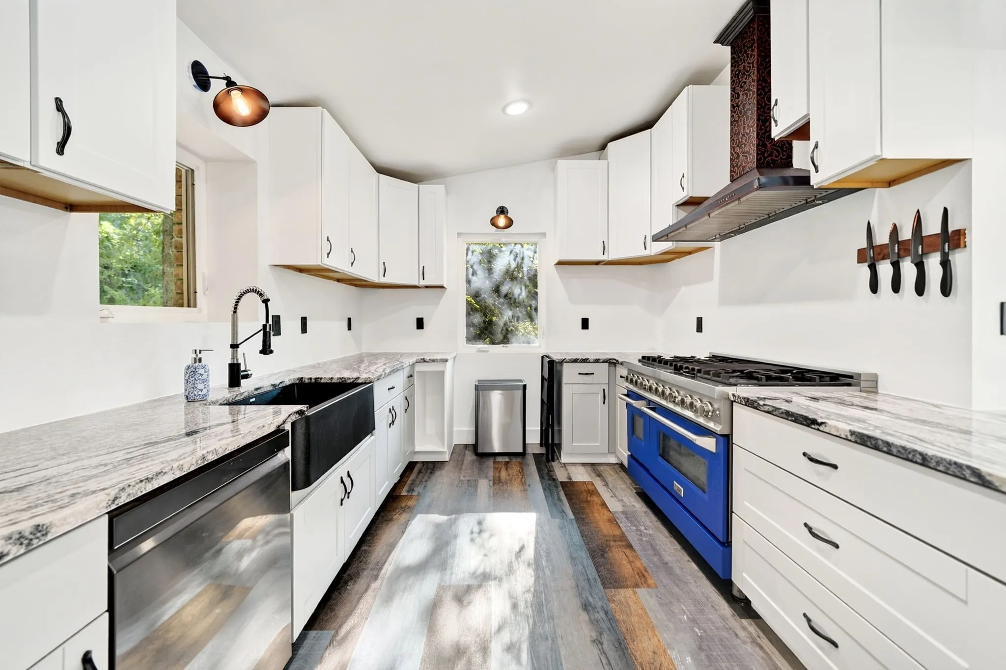 White cabinetry, wood-finish flooring, undermount sink, stainless steel appliances, and stone-finish countertops