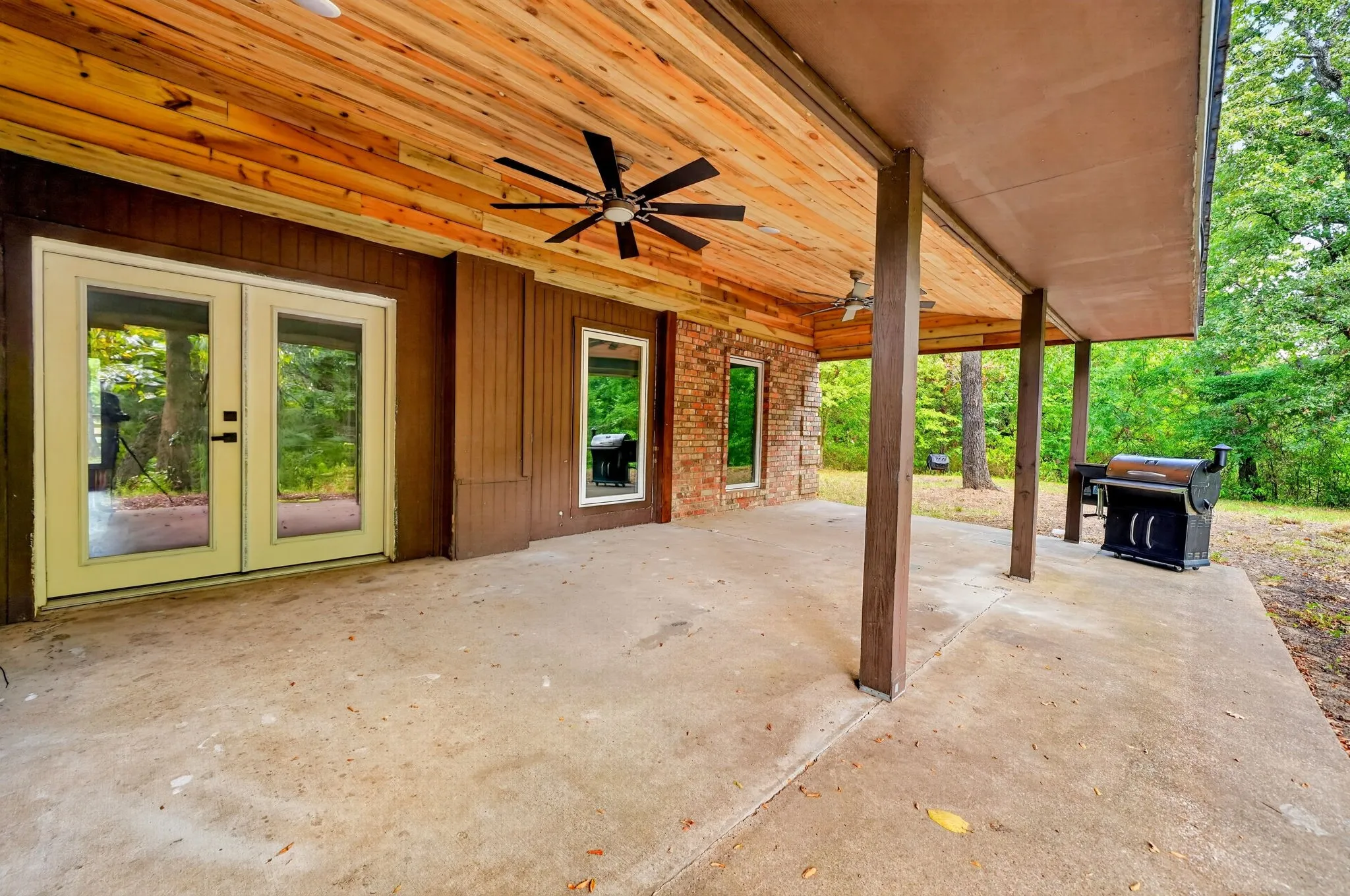 Expansive covered patio featuring a wood-panel ceiling, ceiling fan, and concrete flooring
