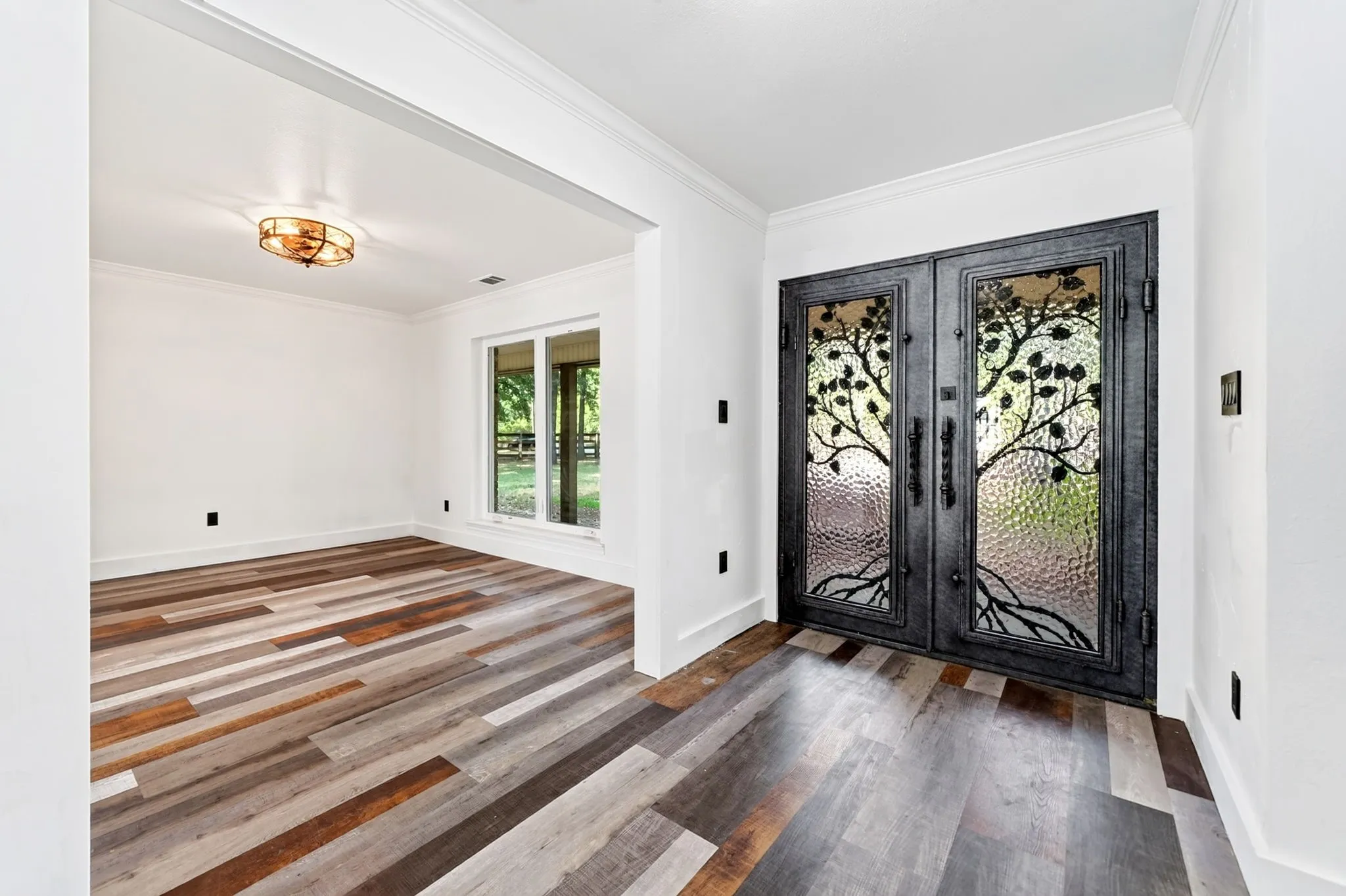Decorative double entry doors with textured glass, wood-finish flooring, and crown molding