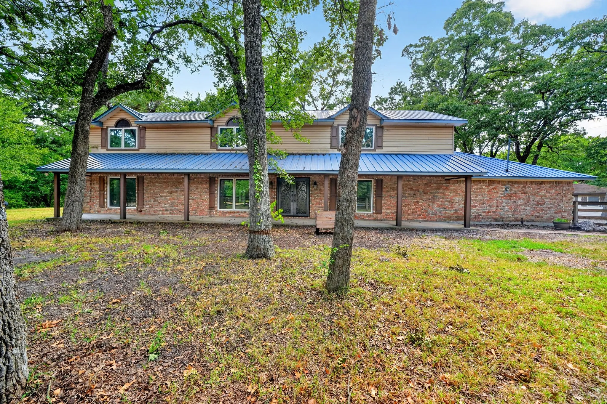 Two-story residence featuring a blue metal roof, brick and siding exterior, front porch with wood columns, and arched dormer windows