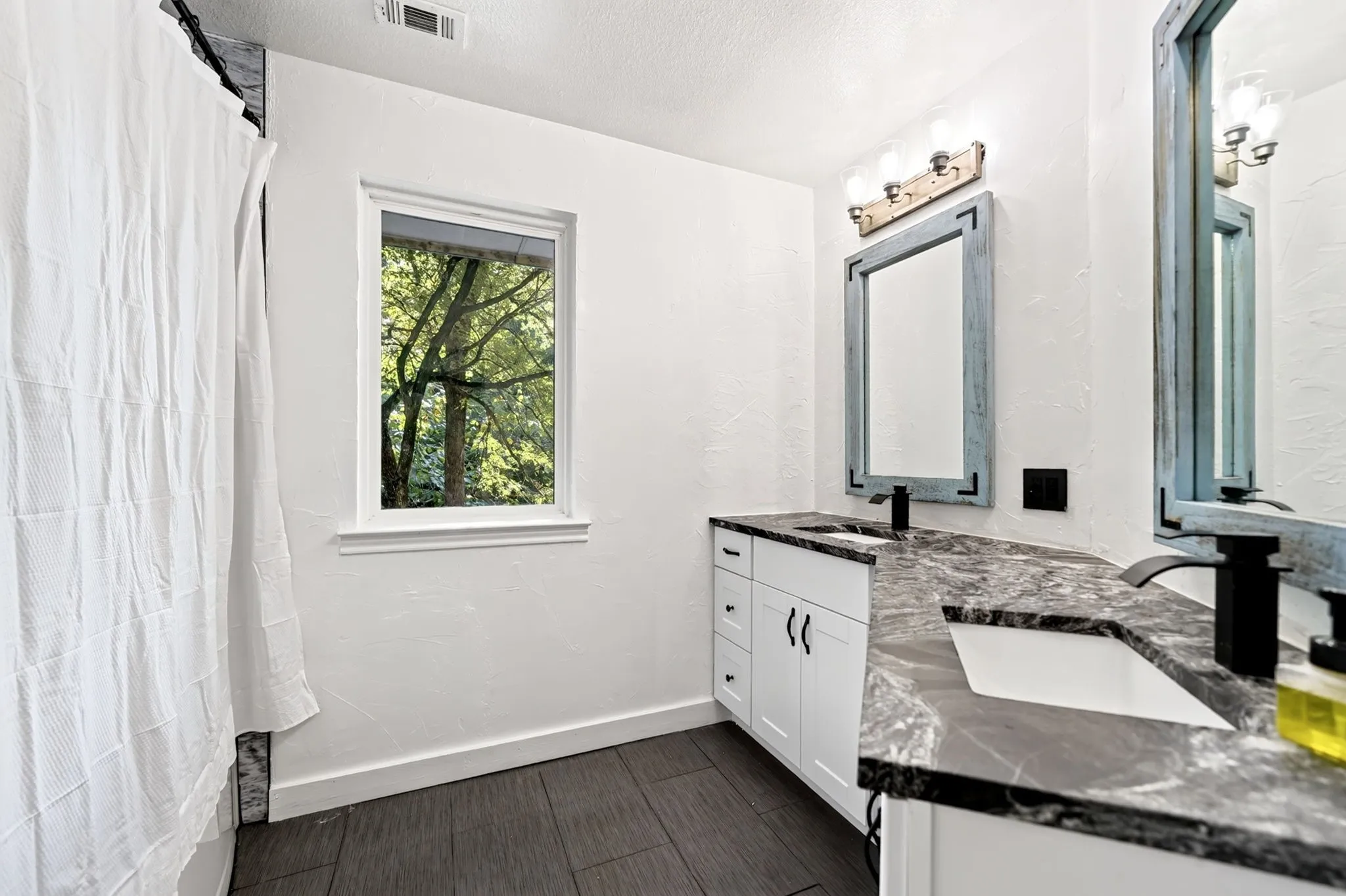 Dual vanity with dark countertops, white cabinetry, and matte black fixtures
