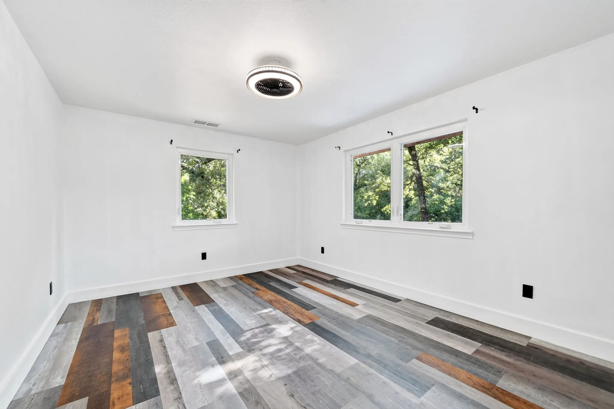 Bright interior with white walls, multi-toned wood-finish flooring, two windows, and a flush-mount ceiling light fixture