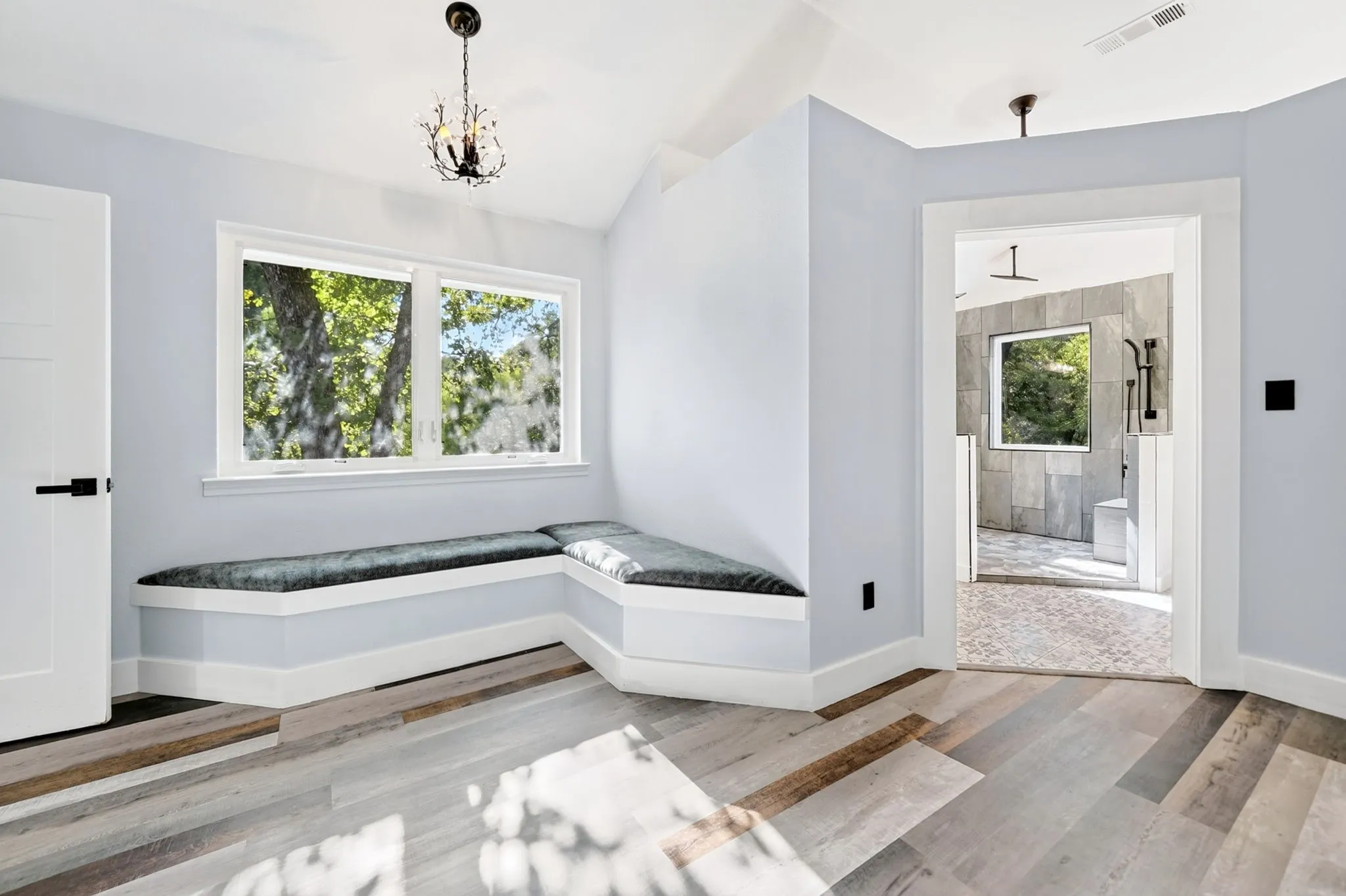 Vaulted ceiling with an ornate chandelier, built-in window seating, wood-finish flooring, and a white interior door with matte black hardware
