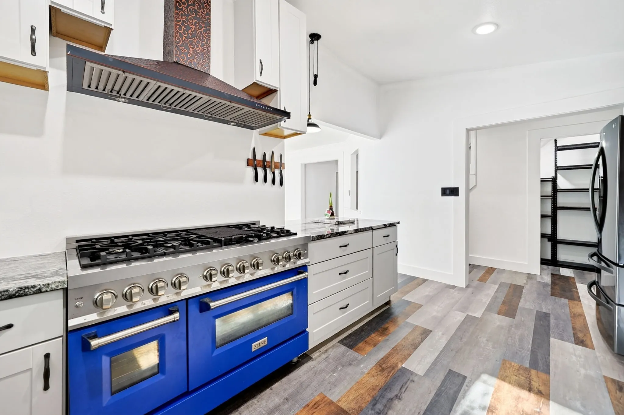 Professional-grade blue range, stainless steel vent hood, white cabinetry, granite countertops, and wood-finish flooring