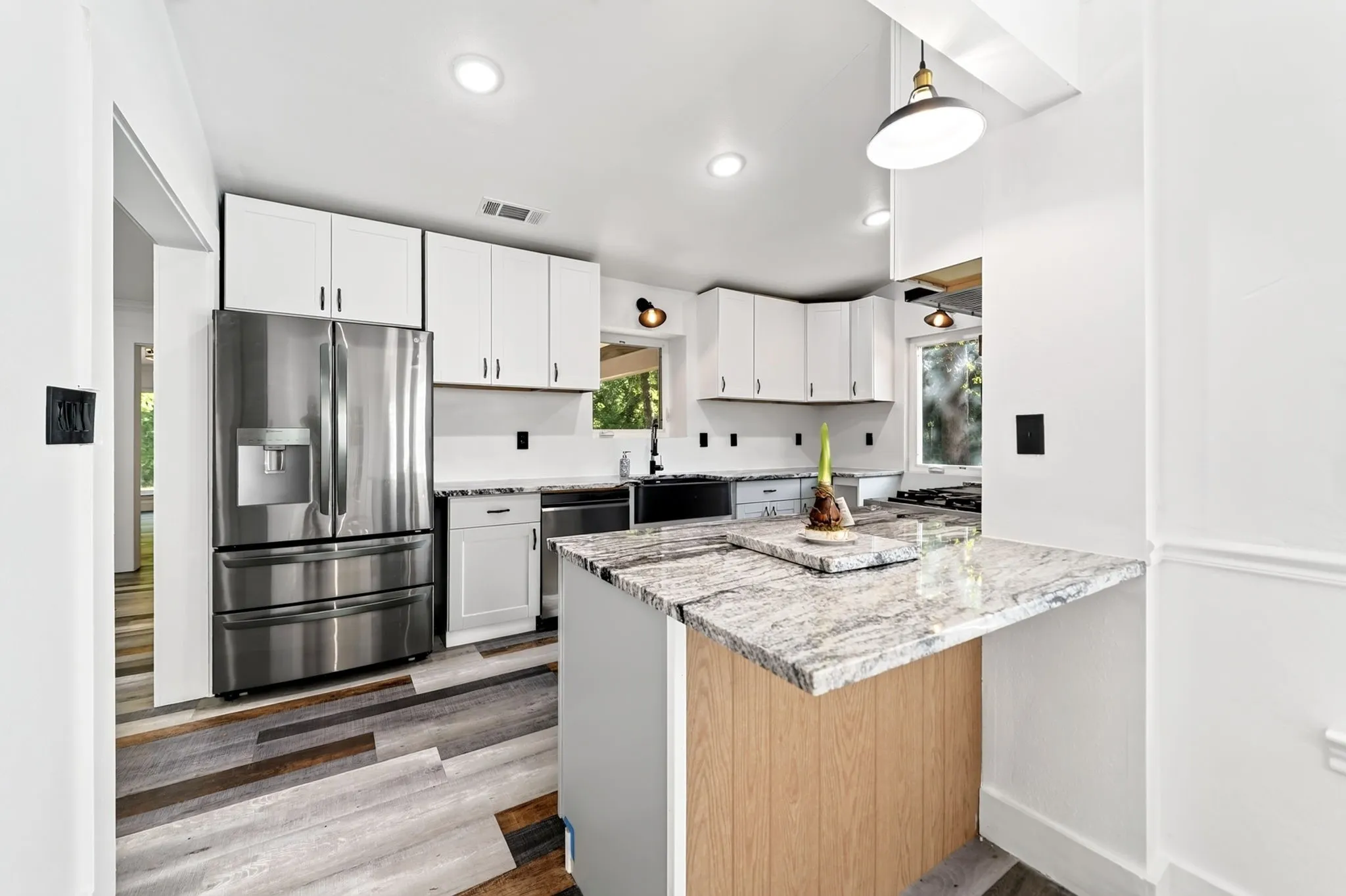 Modern kitchen featuring a stainless steel refrigerator, white cabinetry, recessed lighting, and a multi-level island with light-colored countertops