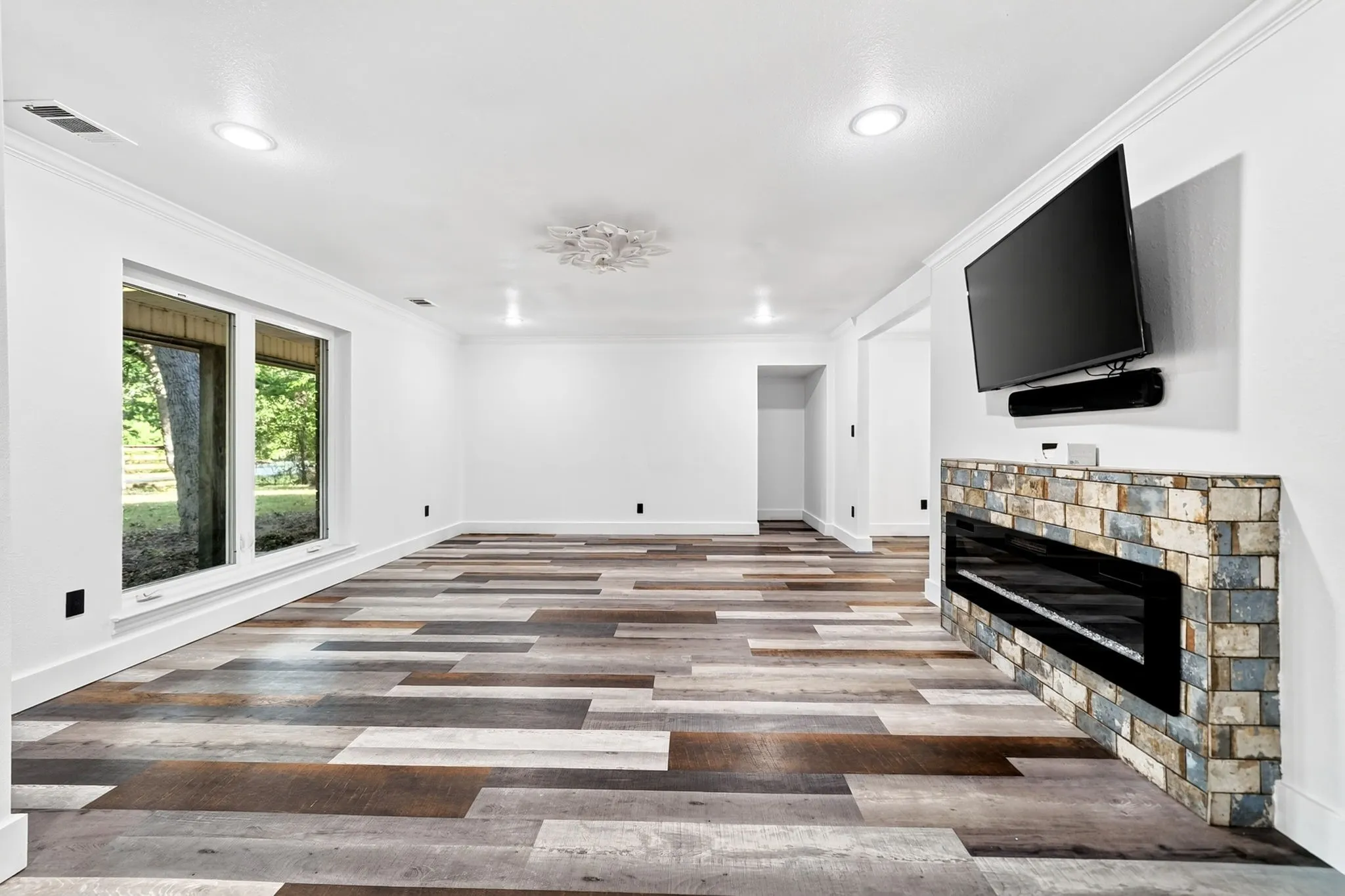 Spacious room featuring multi-toned wood-finish flooring, a contemporary linear fireplace with a stone surround, recessed lighting, and crown molding