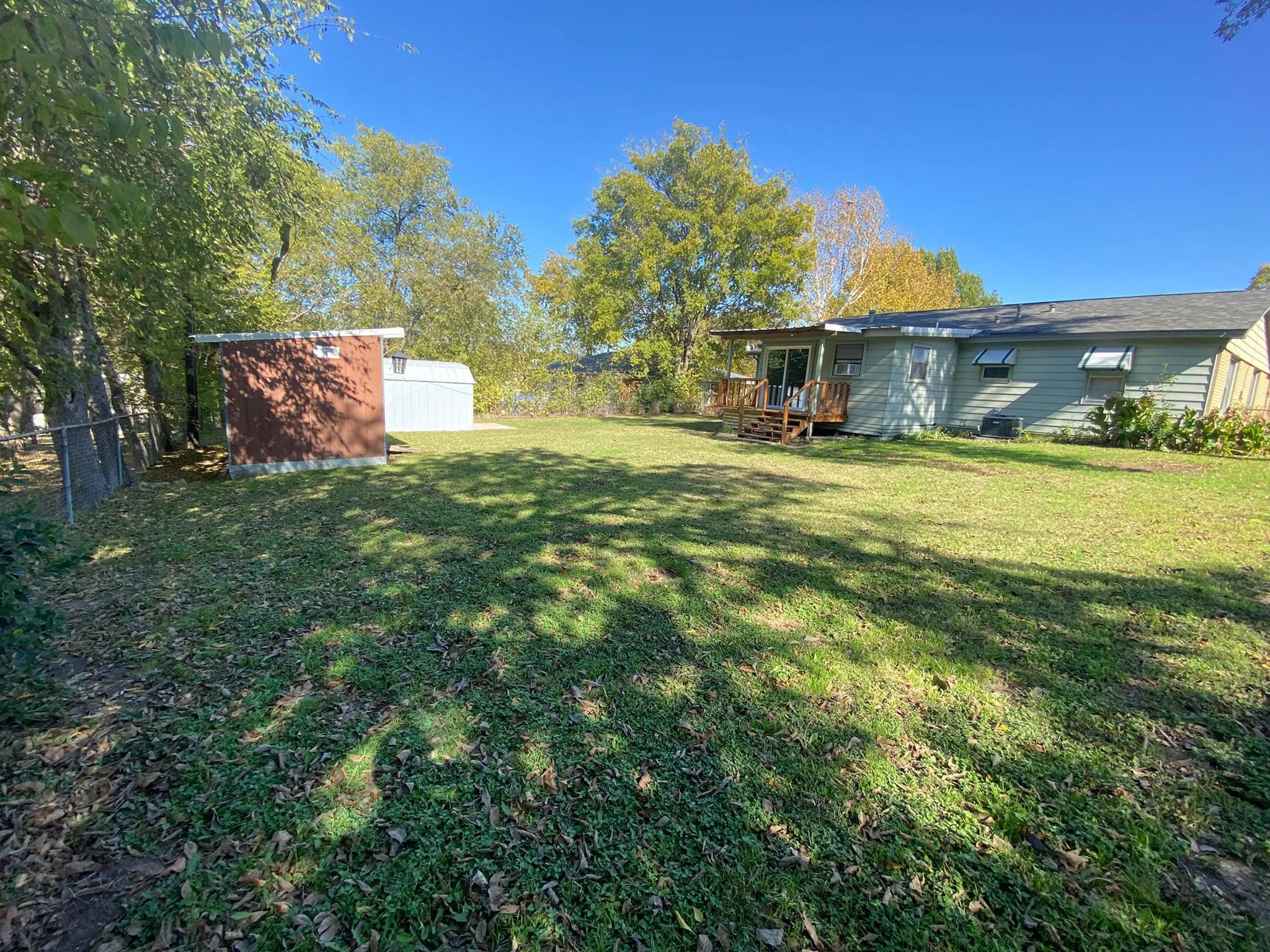 Expansive grassy yard with a chain-link fence, two storage sheds, and a wood deck