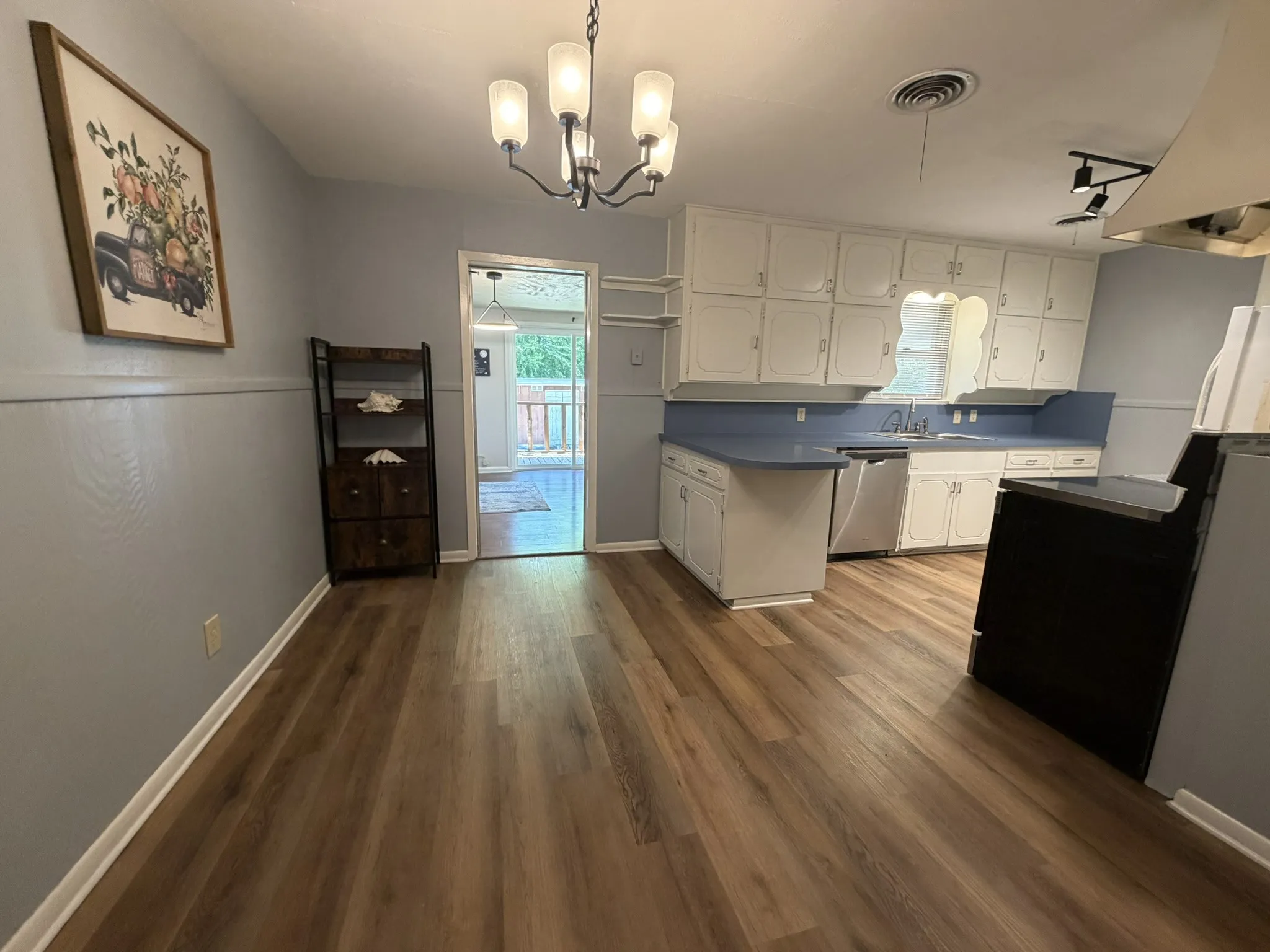 Kitchen and dining area featuring wood-finish flooring, white cabinetry, blue countertops, and a modern chandelier