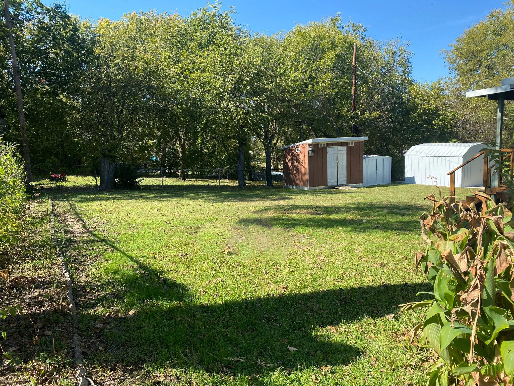 Expansive grassy yard with mature trees, a brown storage shed, and storage sheds