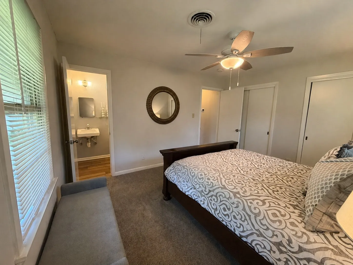Carpeted room with a ceiling fan, windows with blinds, and white bi-fold closet doors and ensuite half bath