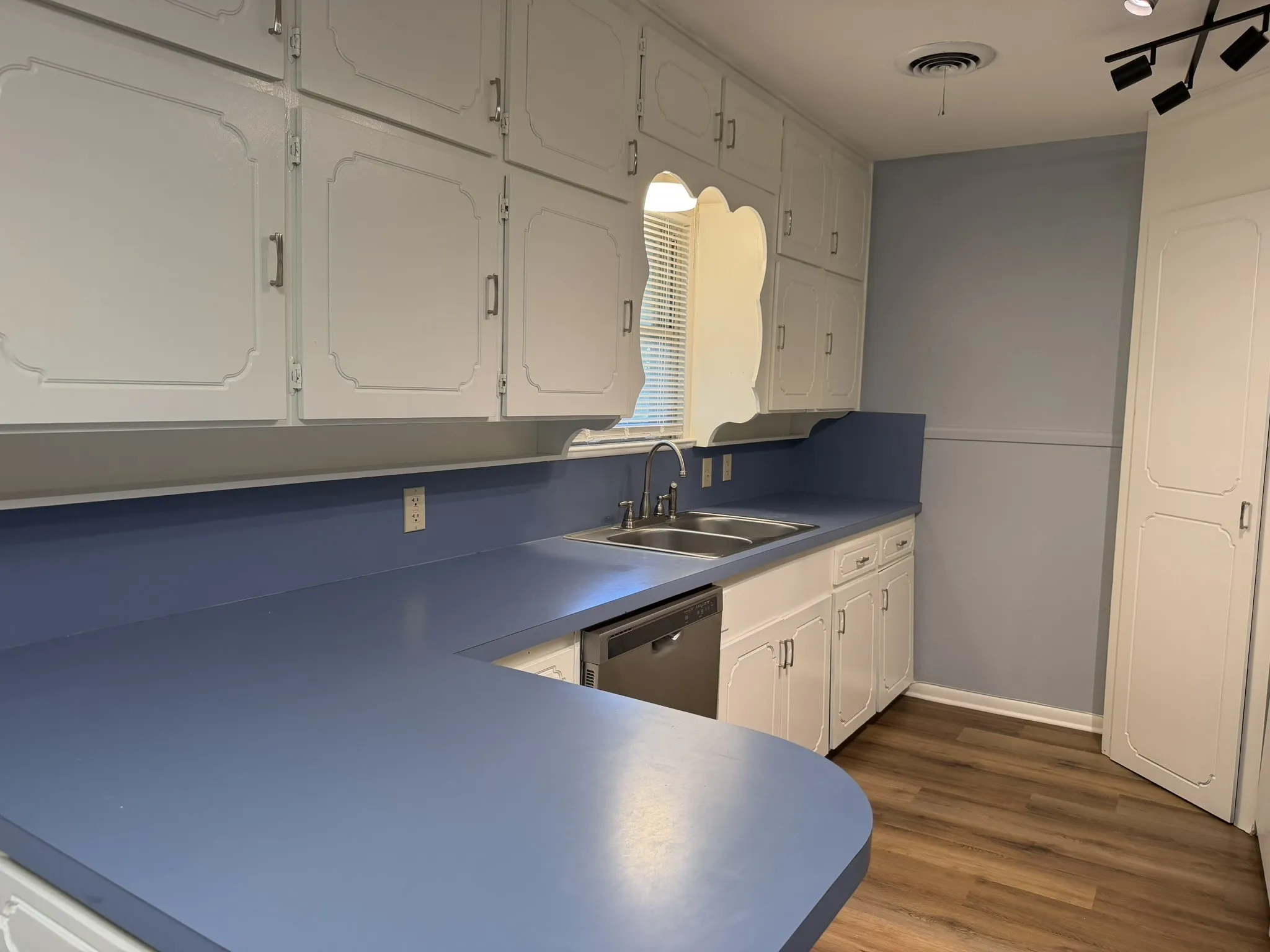 Extensive white cabinetry with decorative trim, blue countertops, stainless steel double basin sink, and wood-finish flooring