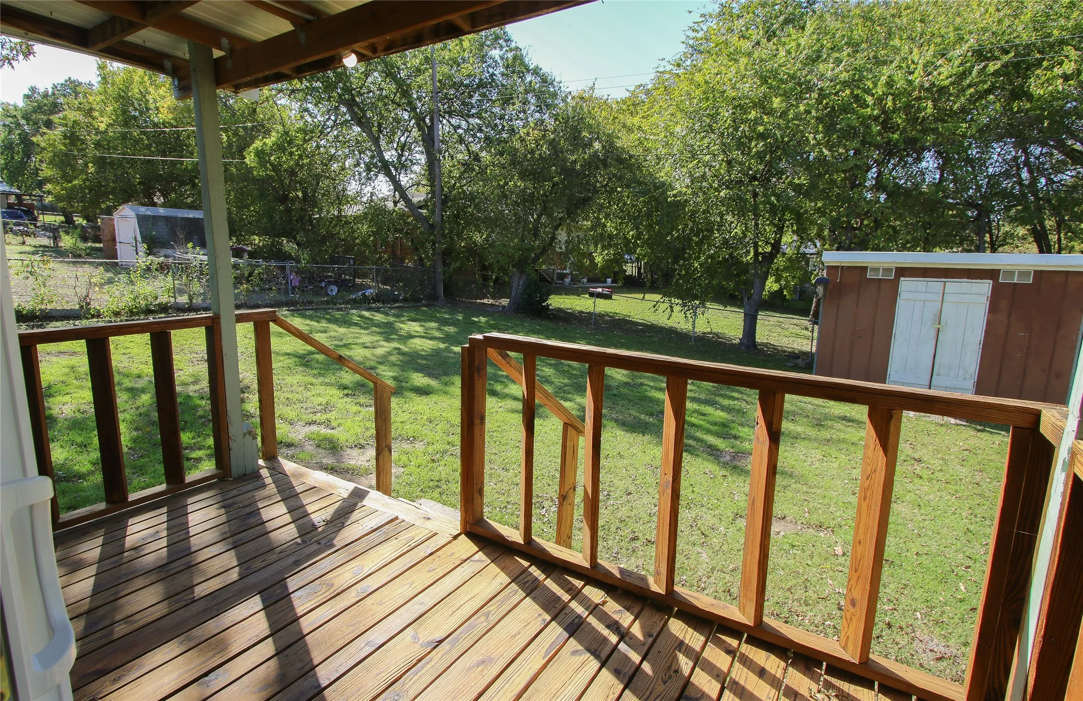 Wood-finish deck with wooden railings, metal roof covering, and a spacious green lawn
