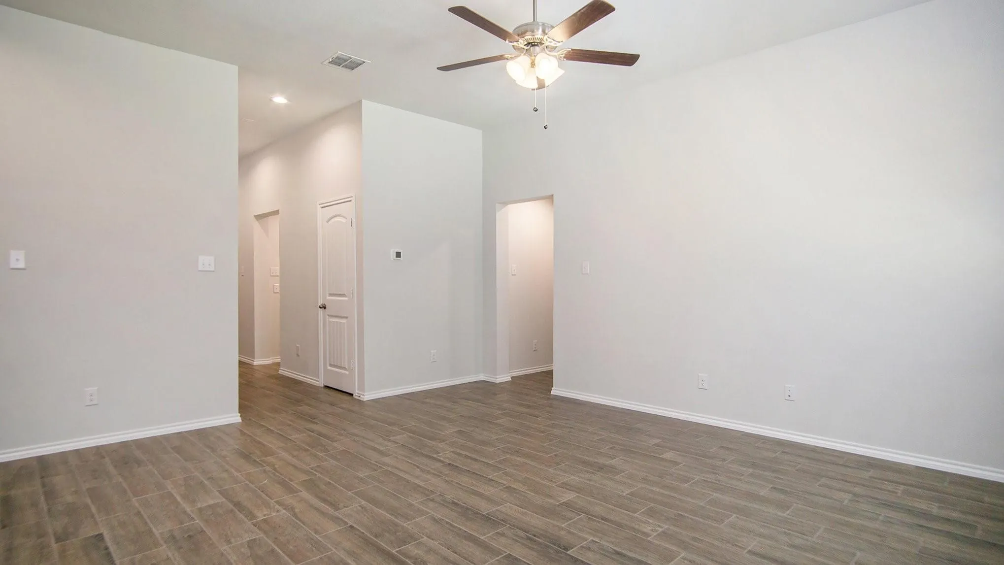Spacious room featuring wood-finish flooring, light neutral wall tones, and white baseboards