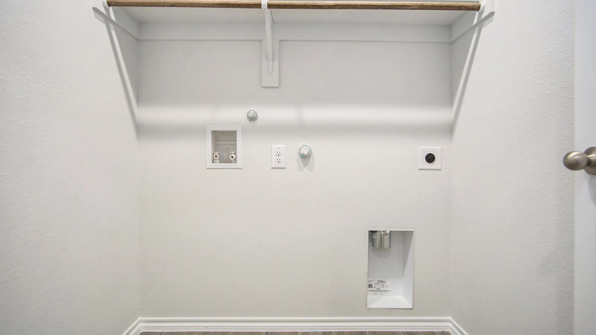 Dedicated utility area featuring a wood-finish hanging rod, white shelving, and essential plumbing and electrical hookups